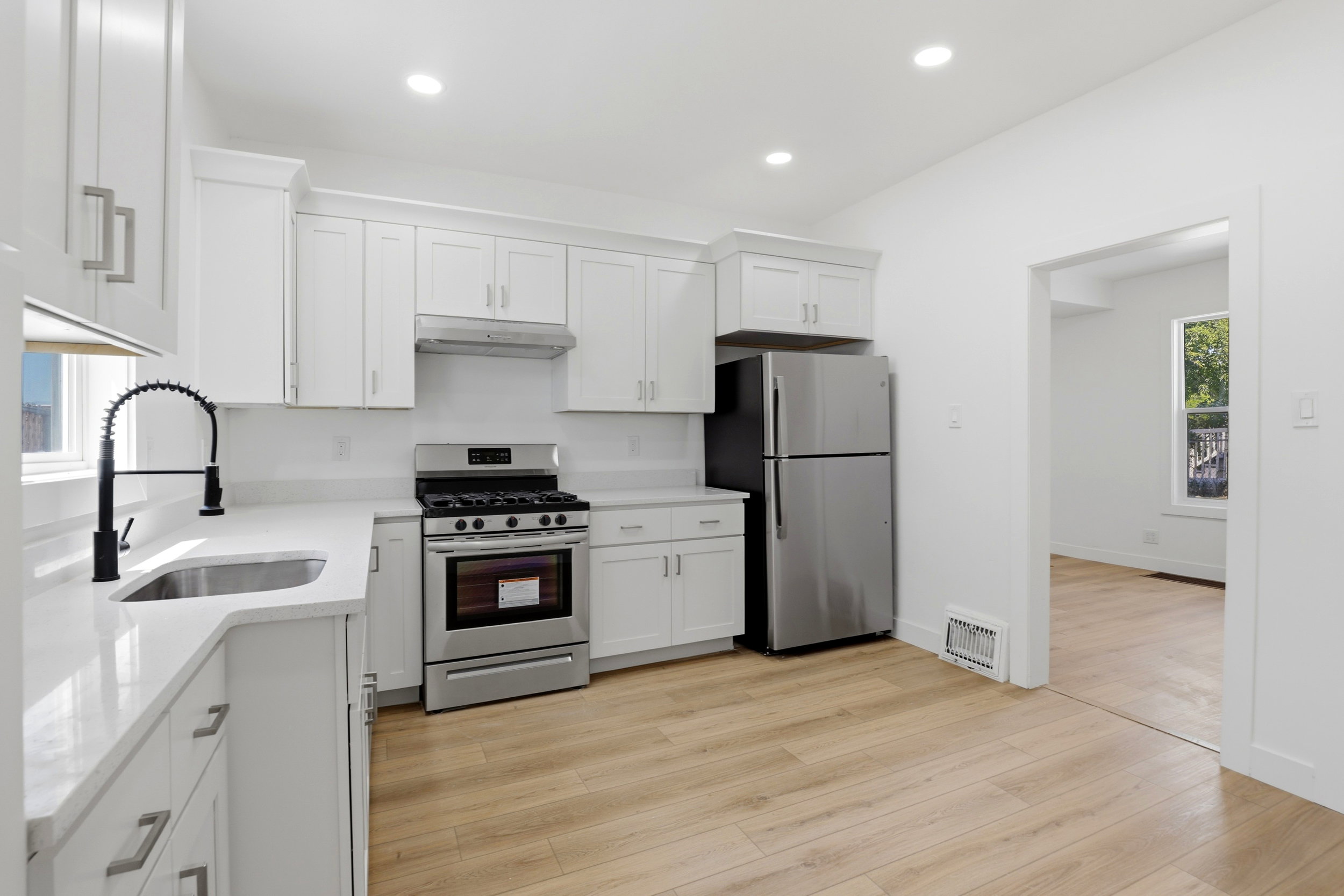 Bright kitchen featuring white shaker cabinetry, stainless steel appliances, light-toned wood-finish flooring, recessed lighting, and a modern black gooseneck faucet