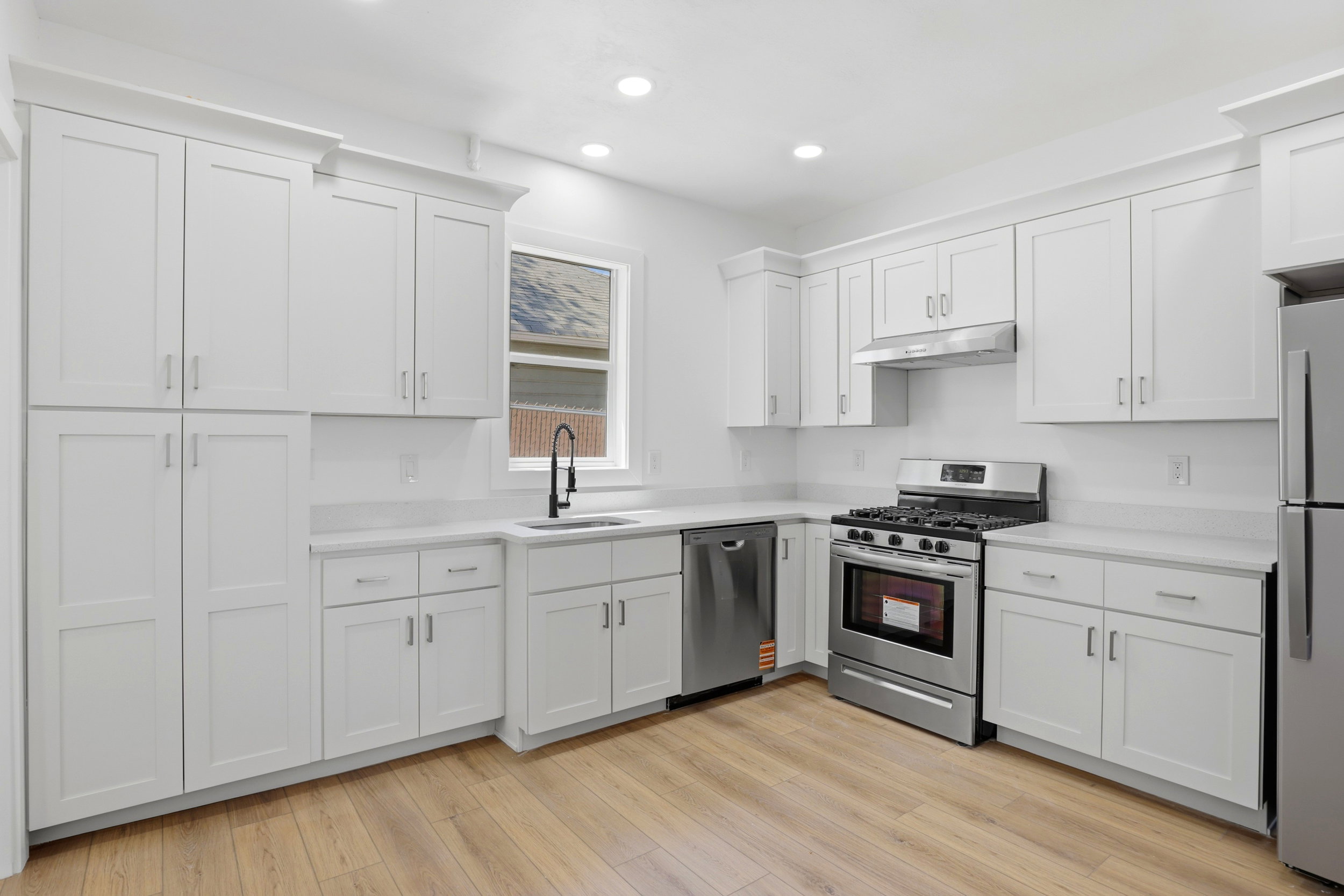 Kitchen featuring extensive white shaker cabinetry, stainless steel appliances, light-toned countertops, a matte black faucet, and wood-finish flooring