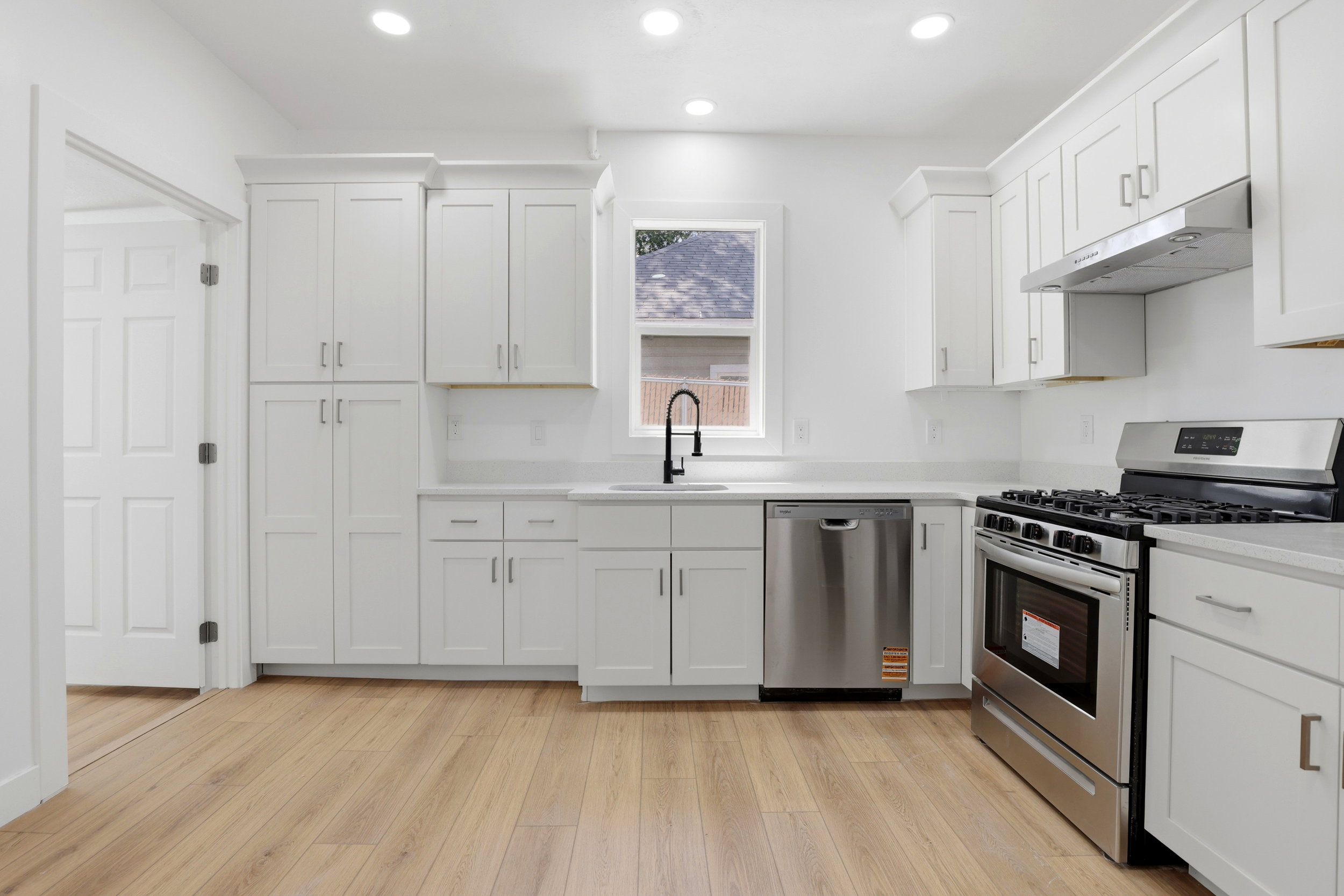Modern kitchen featuring white cabinetry, light-colored countertops, stainless steel appliances, and wood-finish flooring