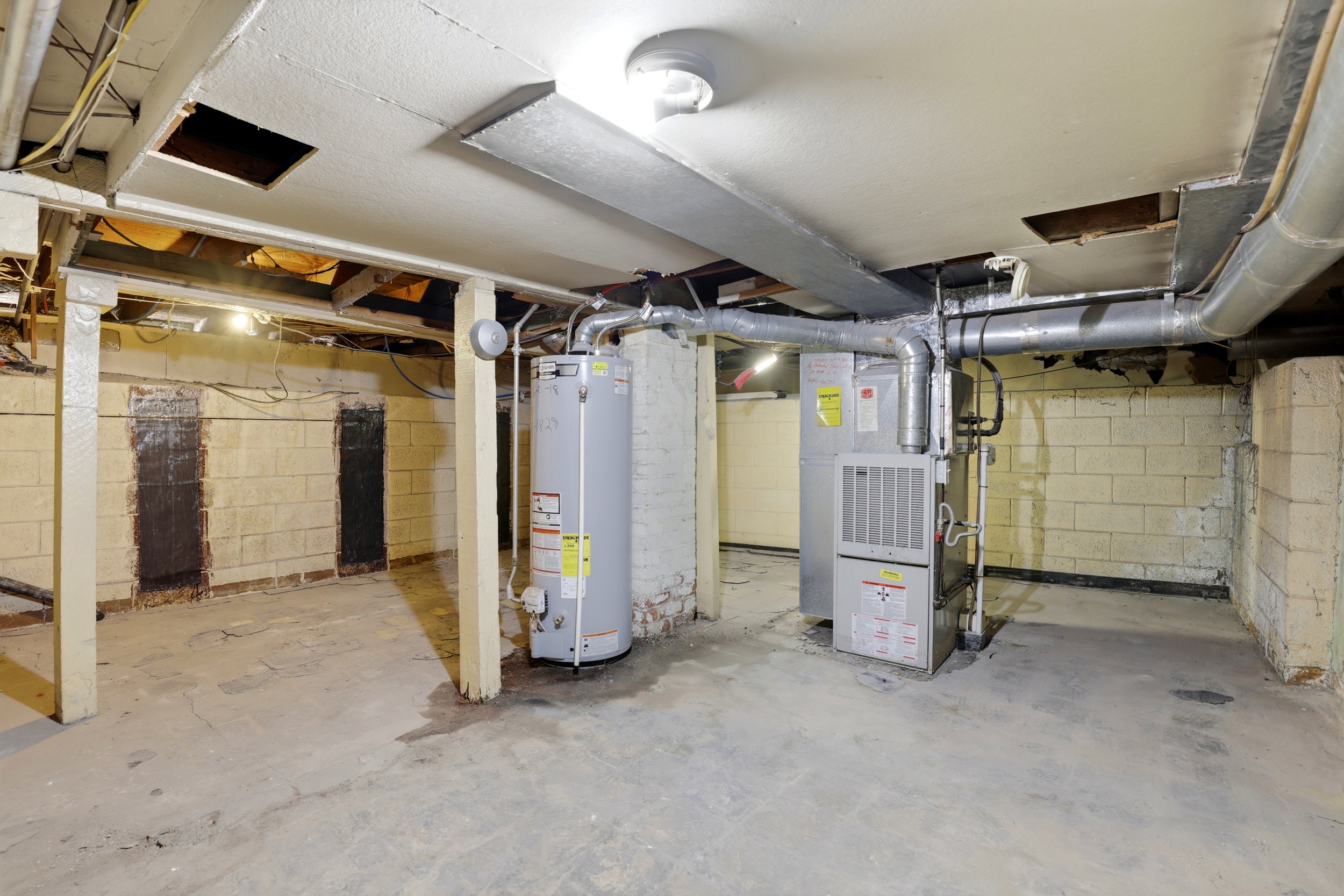Concrete floor basement with exposed ceiling joists, cinder block walls, a water heater, and a furnace