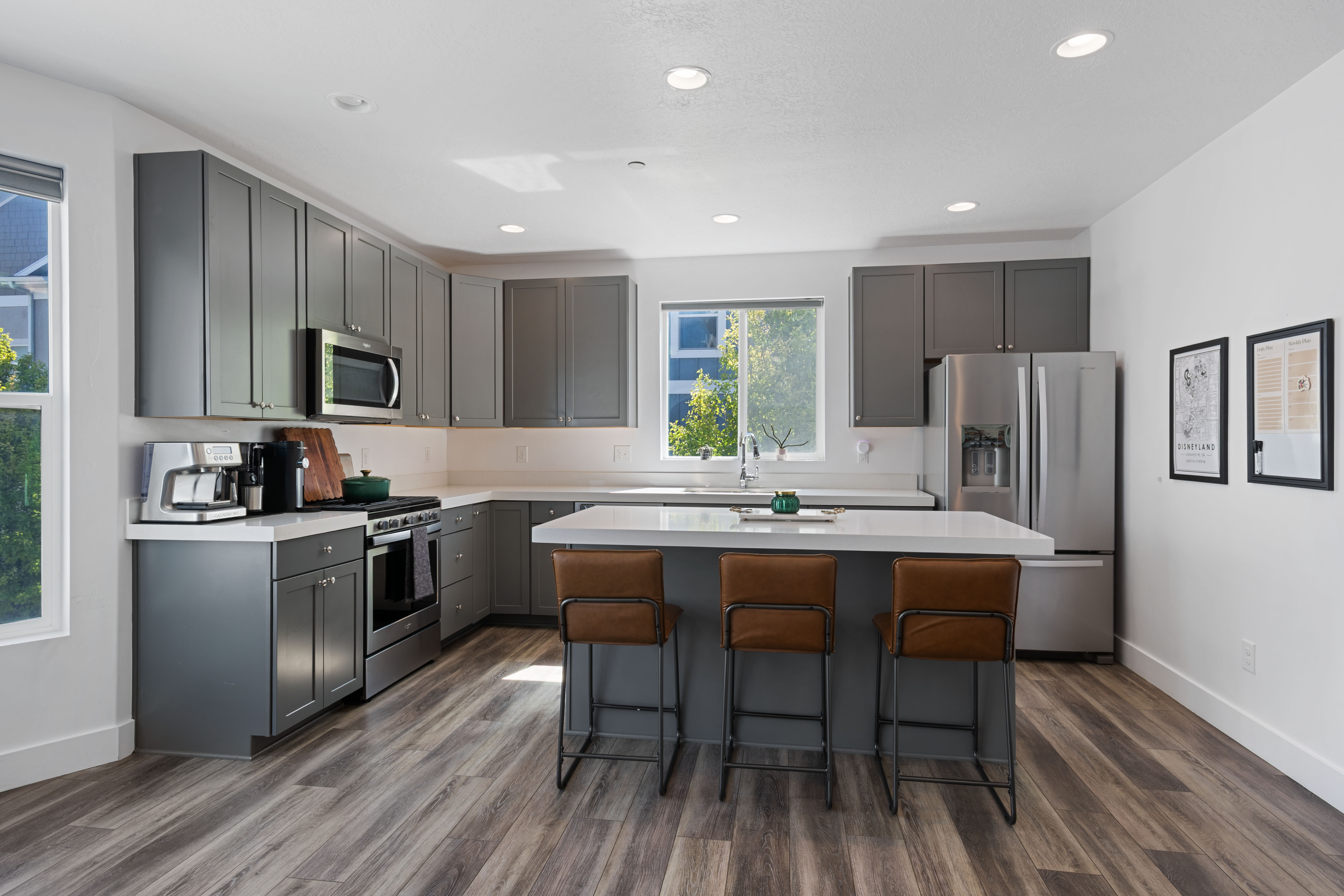 Contemporary kitchen featuring grey cabinetry, stainless steel appliances, light countertops, wood-finish flooring, and recessed lighting
