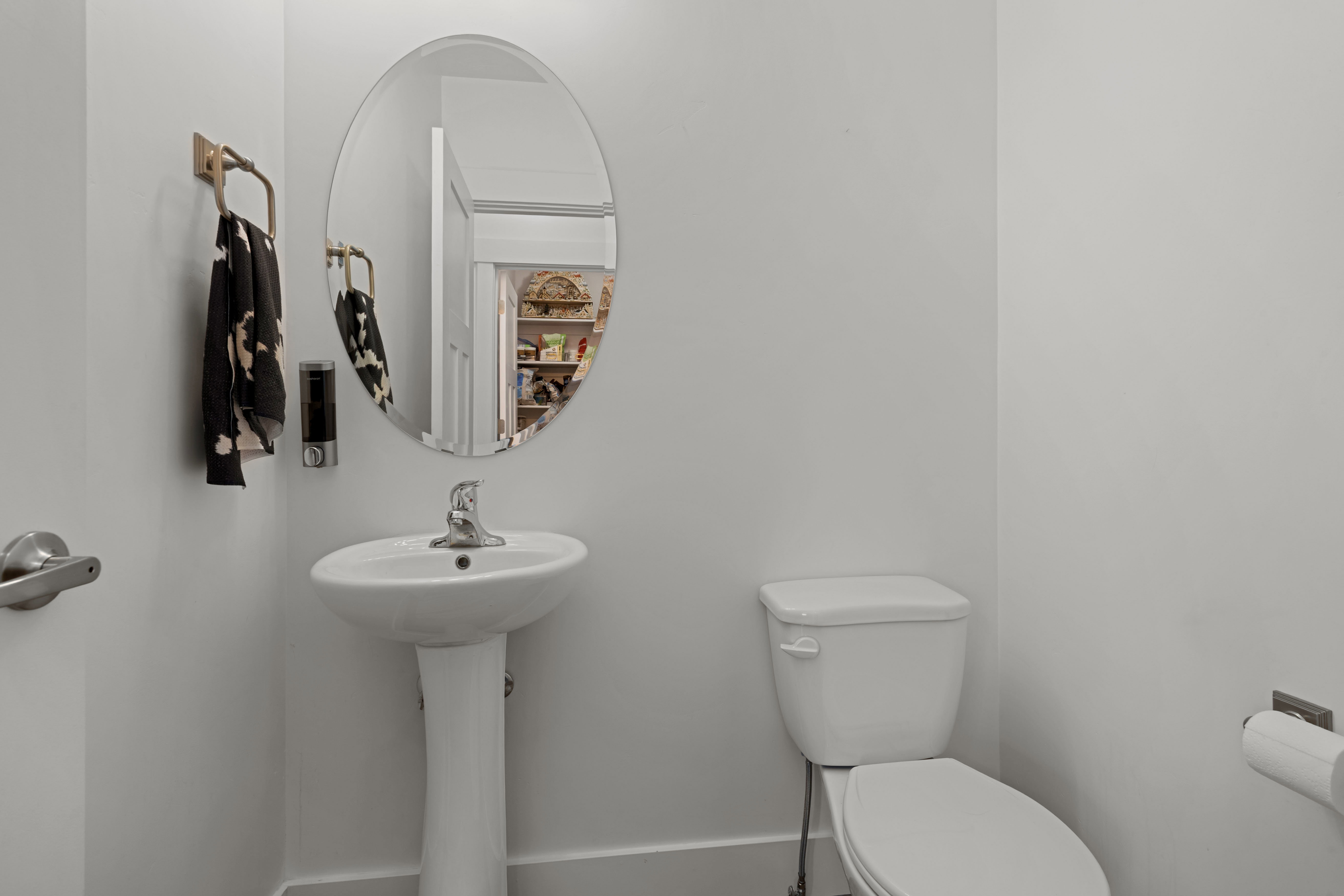 Pedestal sink with chrome faucet, an oval mirror, and a white toilet