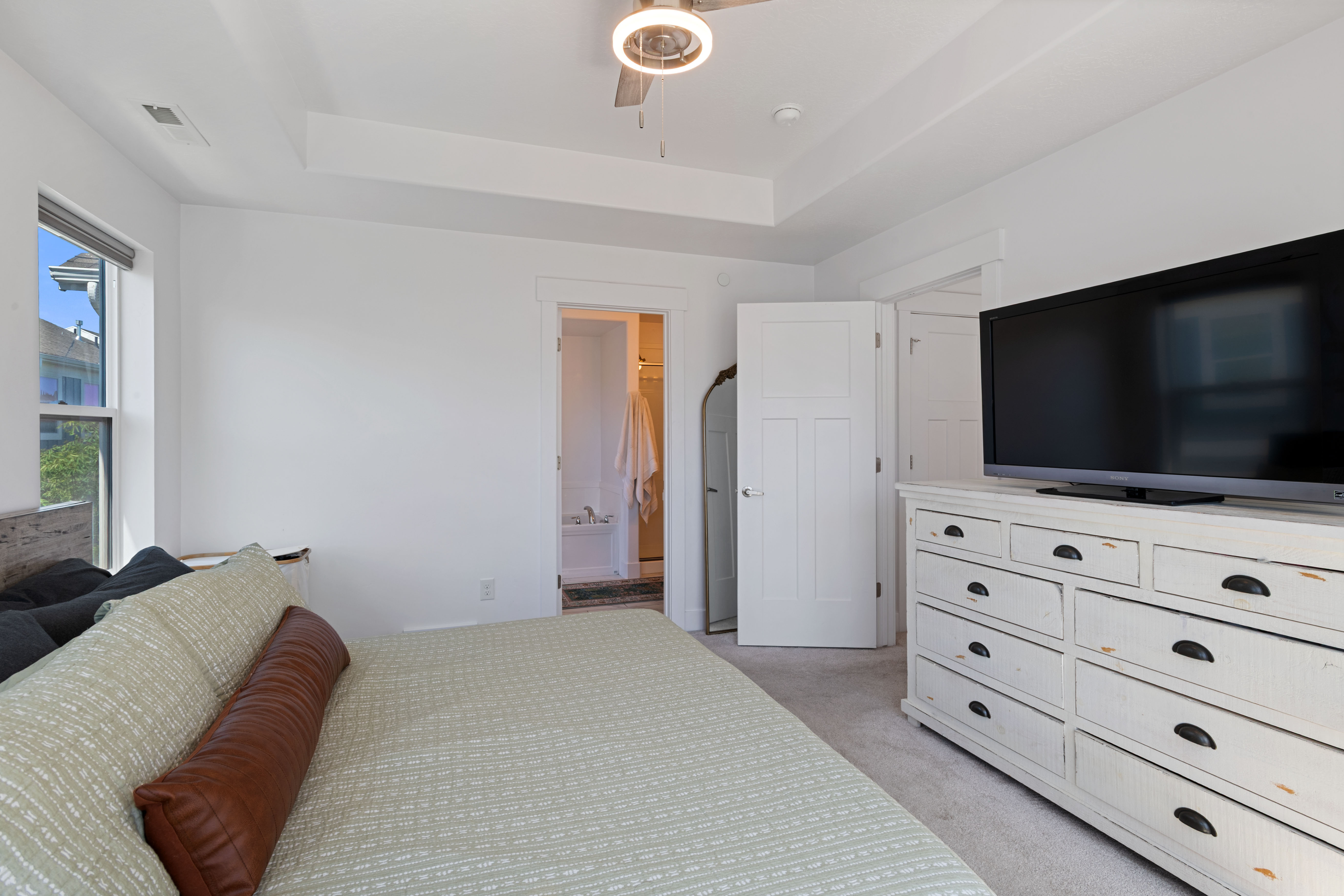 Bright bedroom featuring a tray ceiling with a modern ceiling fan, white walls, and light-toned carpet flooring