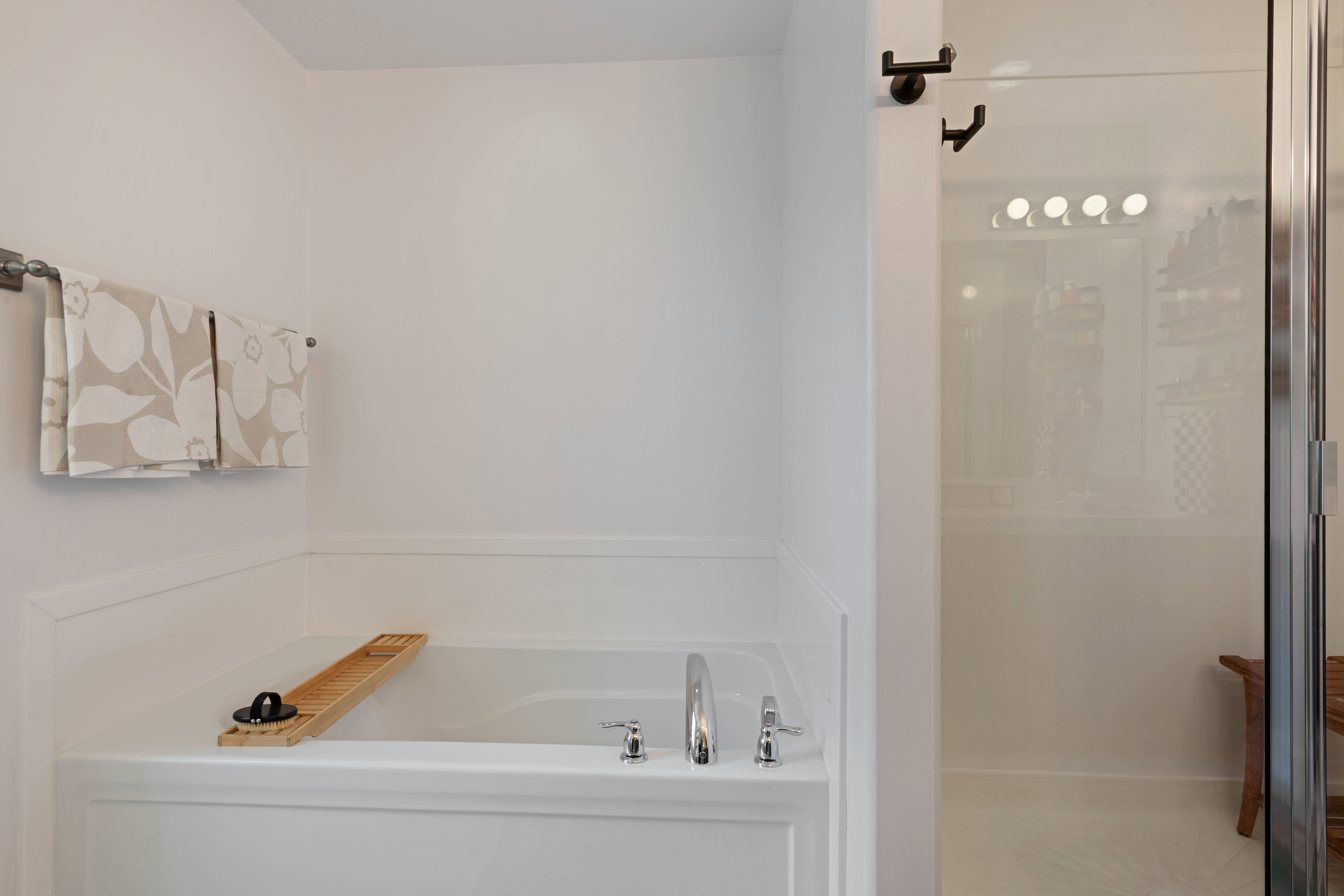 Built-in soaking tub with chrome fixtures complemented by a clear glass-enclosed shower with a multi-bulb light fixture