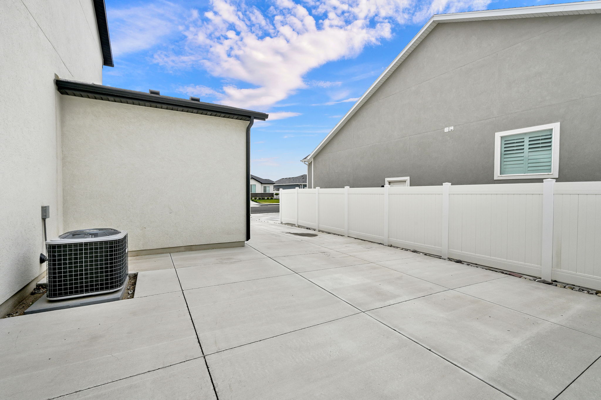 Concrete paving extending alongside the structure, featuring an air conditioning unit and a white privacy fence