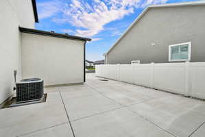 Concrete paving extending alongside the structure, featuring an air conditioning unit and a white privacy fence