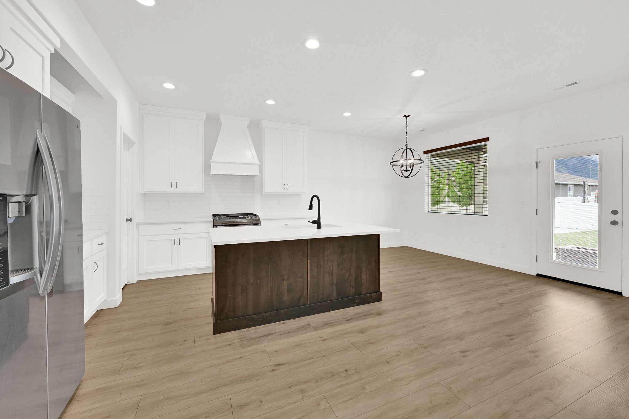 Kitchen featuring white cabinetry, subway tile backsplash, a dark wood-finish island with a white countertop, stainless steel appliances, and light wood-finish flooring