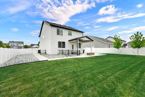 Expansive backyard featuring a large green lawn, concrete patio, covered outdoor living space, and white privacy fencing