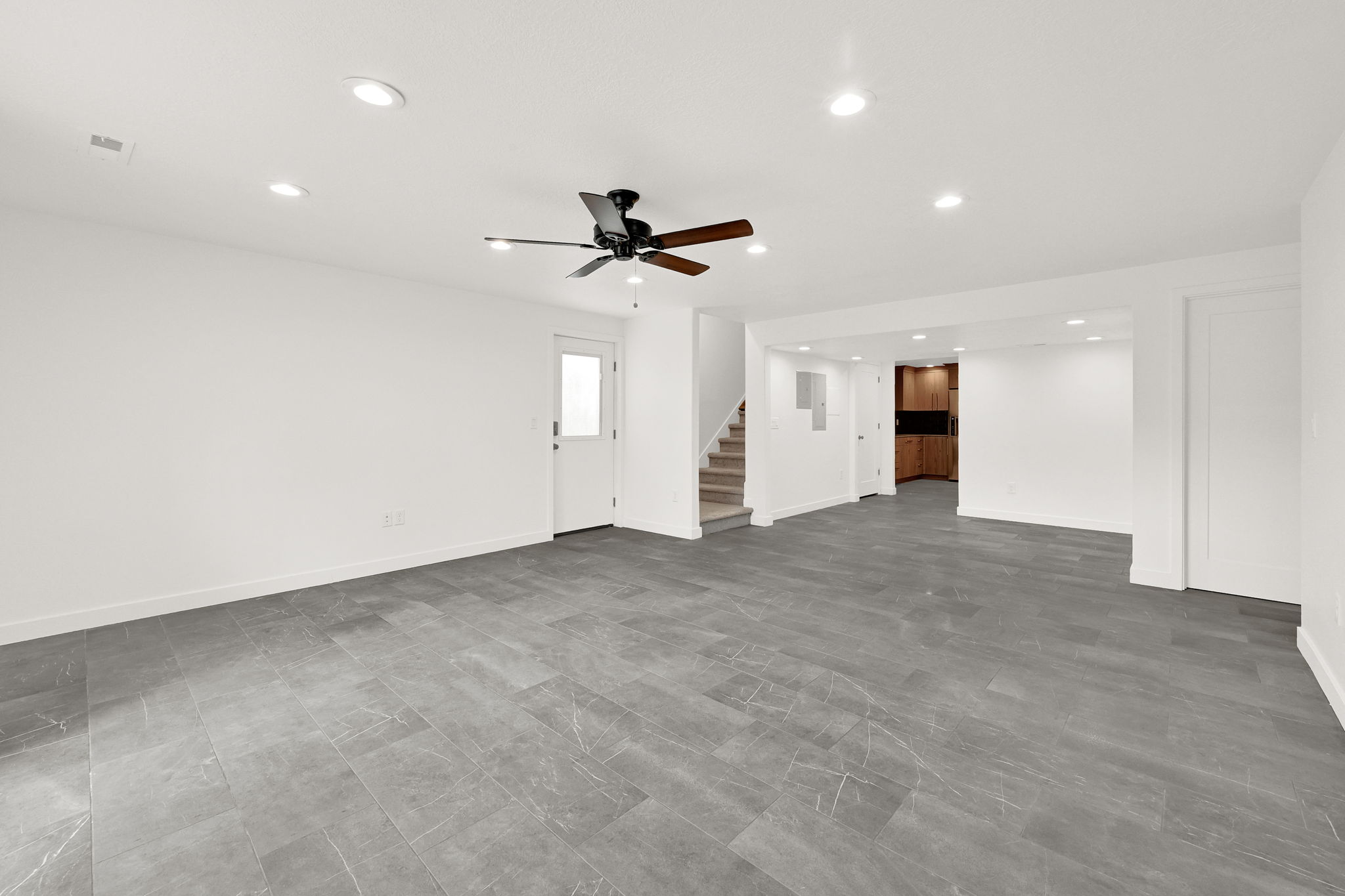 Spacious room featuring large format grey tile flooring, white walls, and recessed lighting