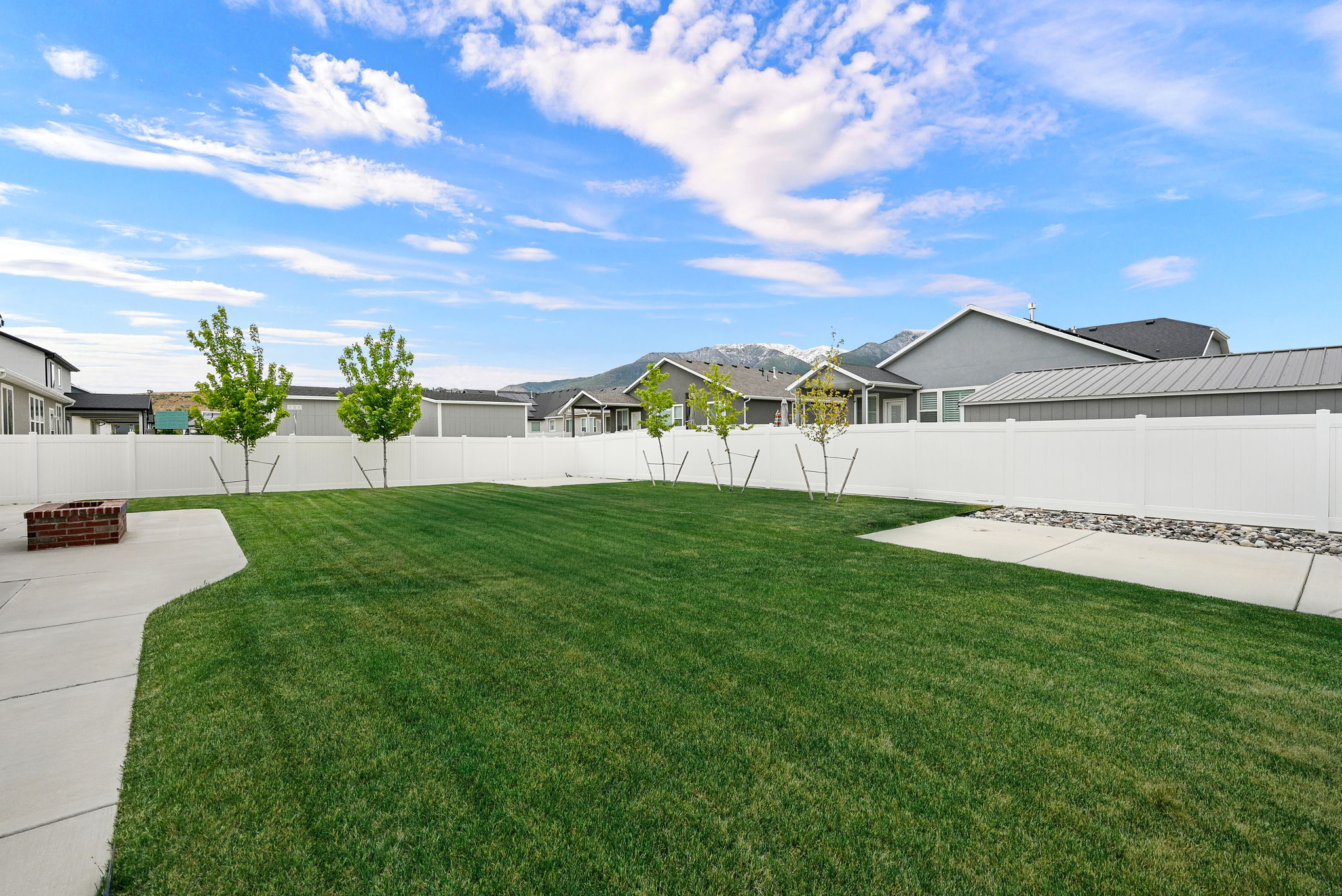 Expansive backyard featuring a large green lawn, concrete patio, and a built-in brick fire pit