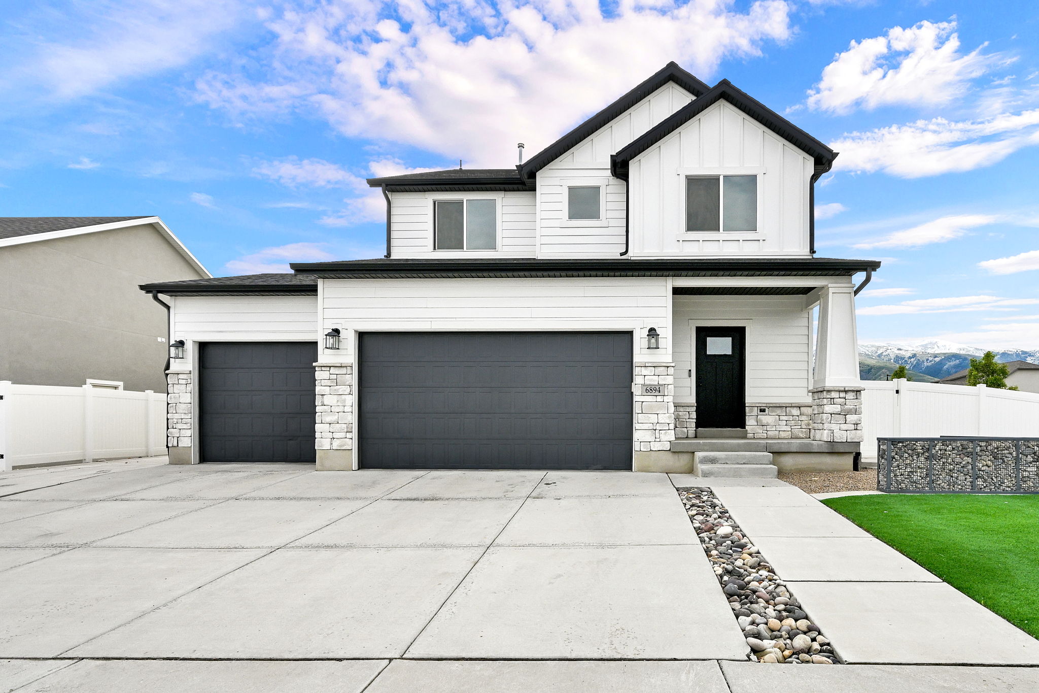 Contemporary two-story residence featuring white siding, a contrasting dark roof, and stone facade accents