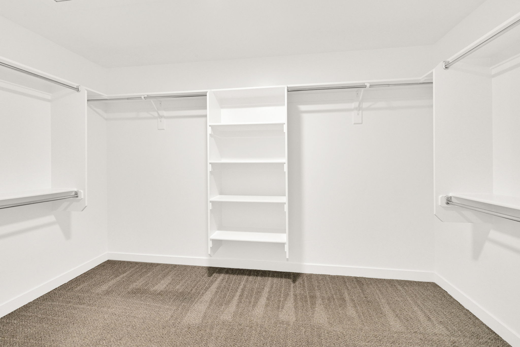 Walk-in closet featuring built-in white shelving, multiple hanging rods, and neutral carpet flooring