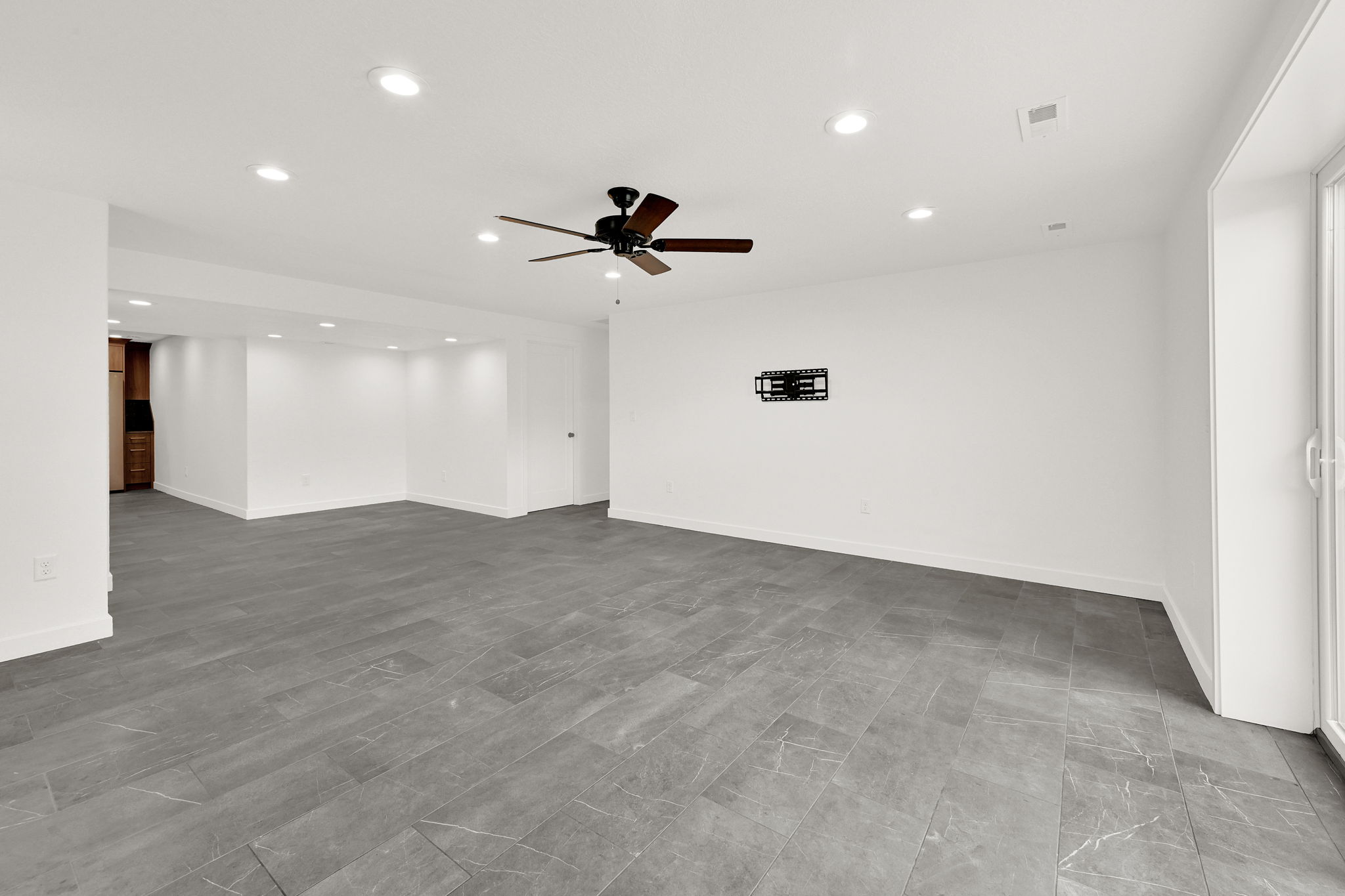 Spacious room featuring large format grey tile flooring, white walls, recessed lighting, and a ceiling fan