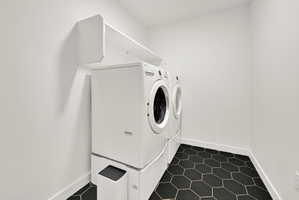 Dedicated laundry area featuring a white front-load washer and dryer set, elevated on pedestals, with overhead shelving and a hexagonal tile floor