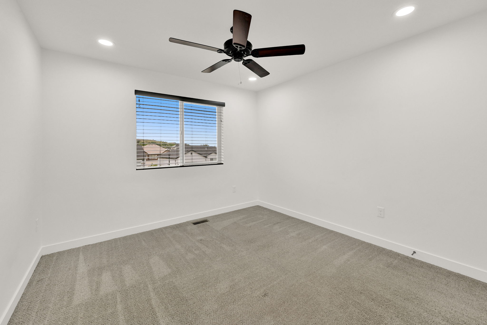 Carpeted interior space featuring a window with horizontal blinds, a dark-toned ceiling fan, and recessed ceiling lighting