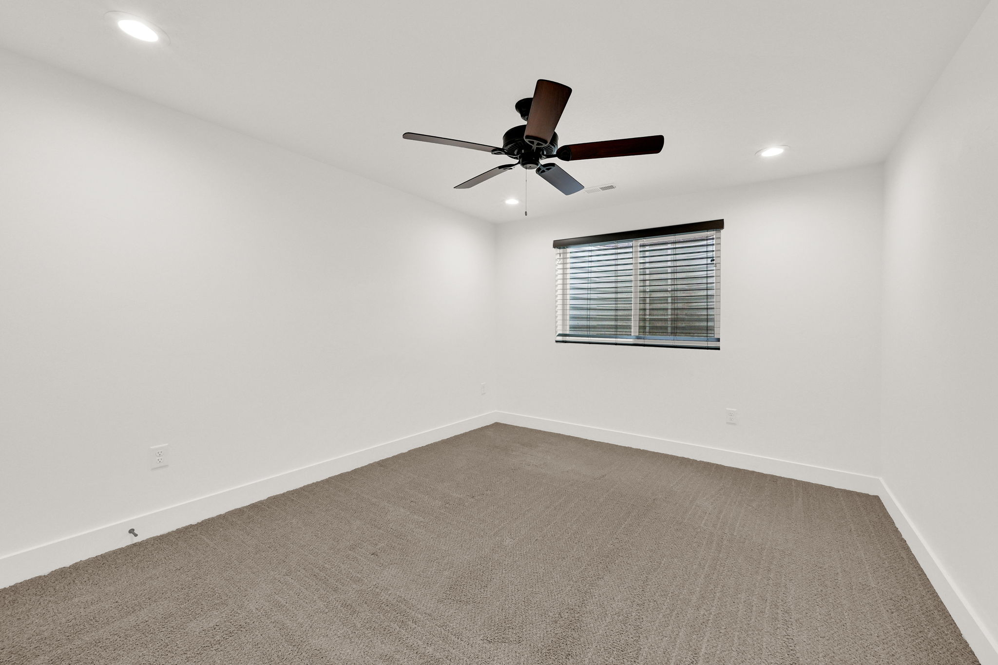 Spacious room featuring neutral carpeting, white walls, recessed lighting, a ceiling fan, and a window with blinds