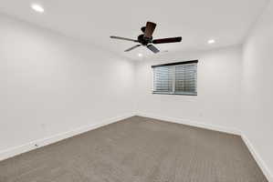 Spacious room featuring neutral carpeting, white walls, recessed lighting, a ceiling fan, and a window with blinds