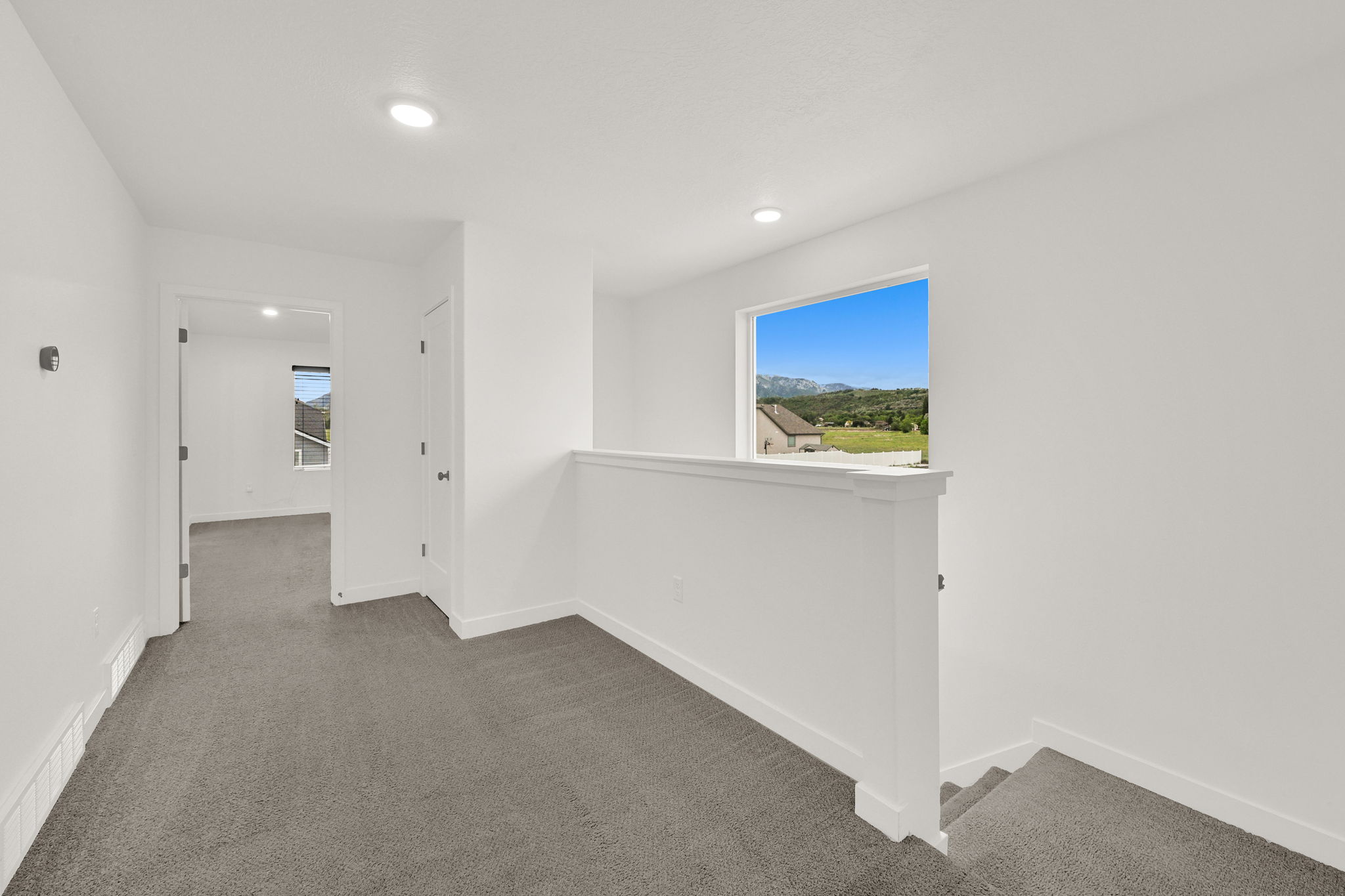 Upper-level hallway with neutral carpeting, recessed lighting, white trim, and a window offering a mountain and landscape backdrop