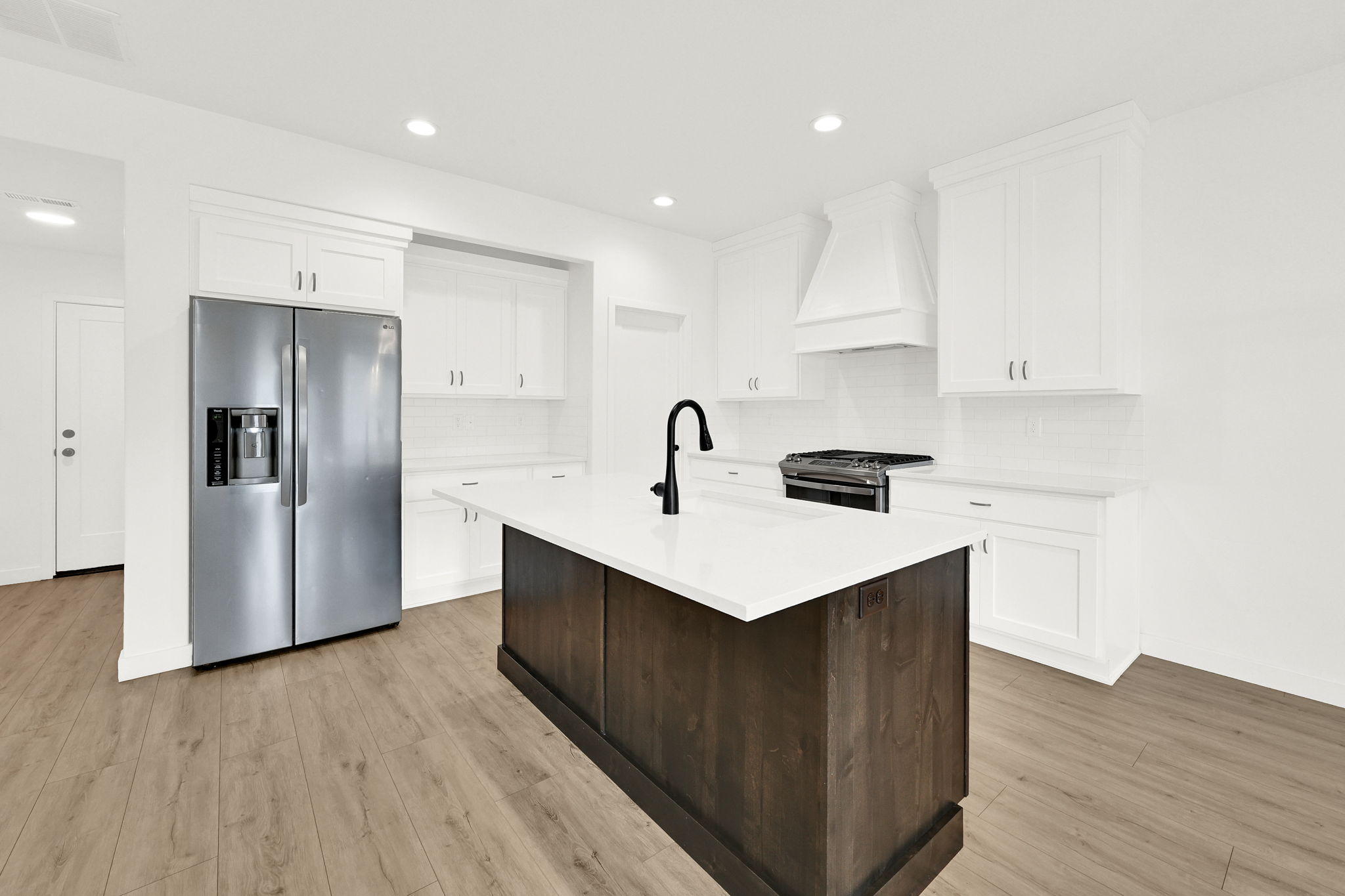 Kitchen featuring a dark wood-finish island with a white countertop, contrasting with white perimeter cabinetry and subway tile backsplash