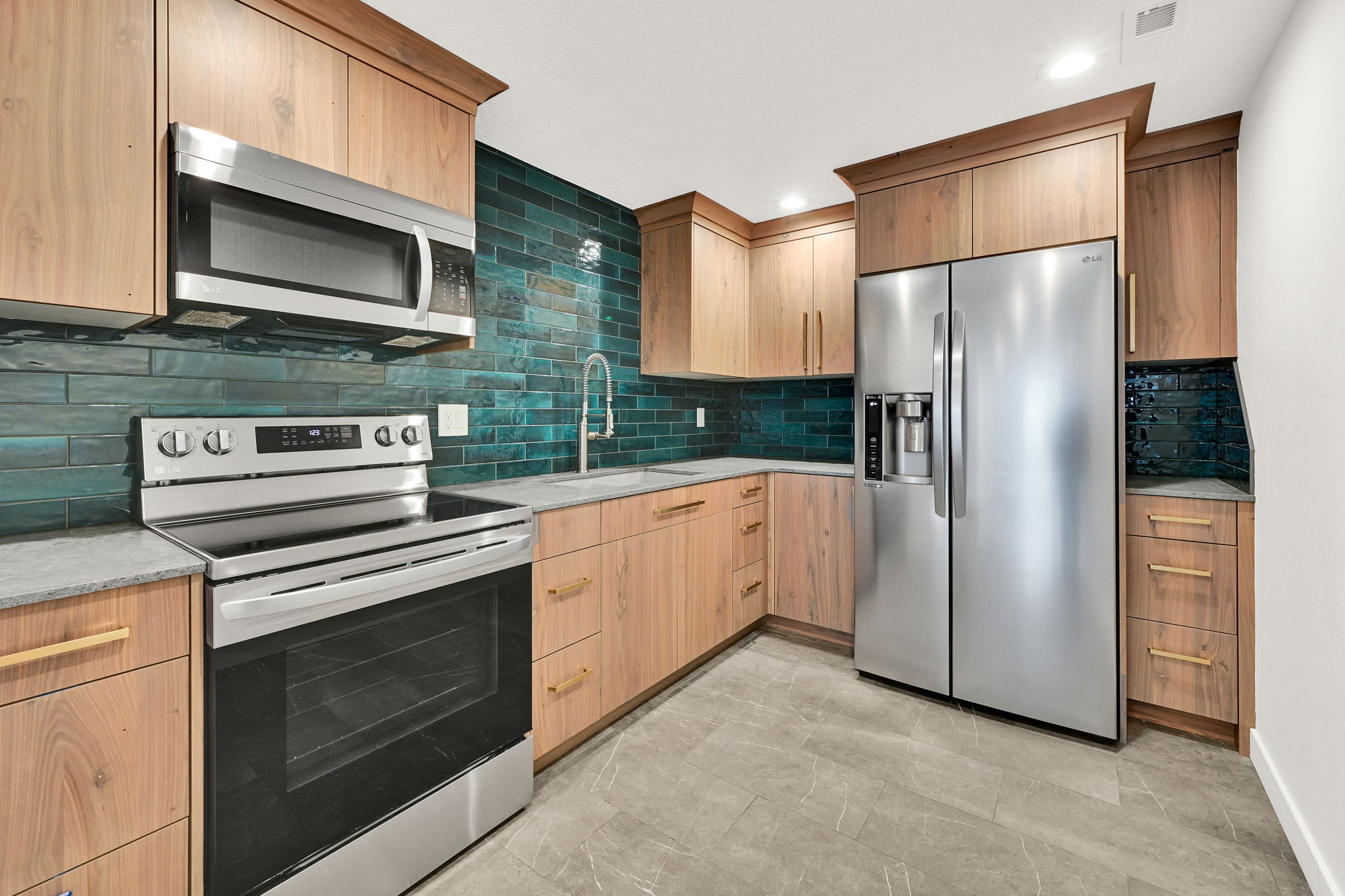 Contemporary kitchen featuring rich wood cabinetry, stainless steel appliances, a striking green subway tile backsplash, and light gray countertops