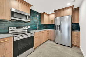 Contemporary kitchen featuring rich wood cabinetry, stainless steel appliances, a striking green subway tile backsplash, and light gray countertops