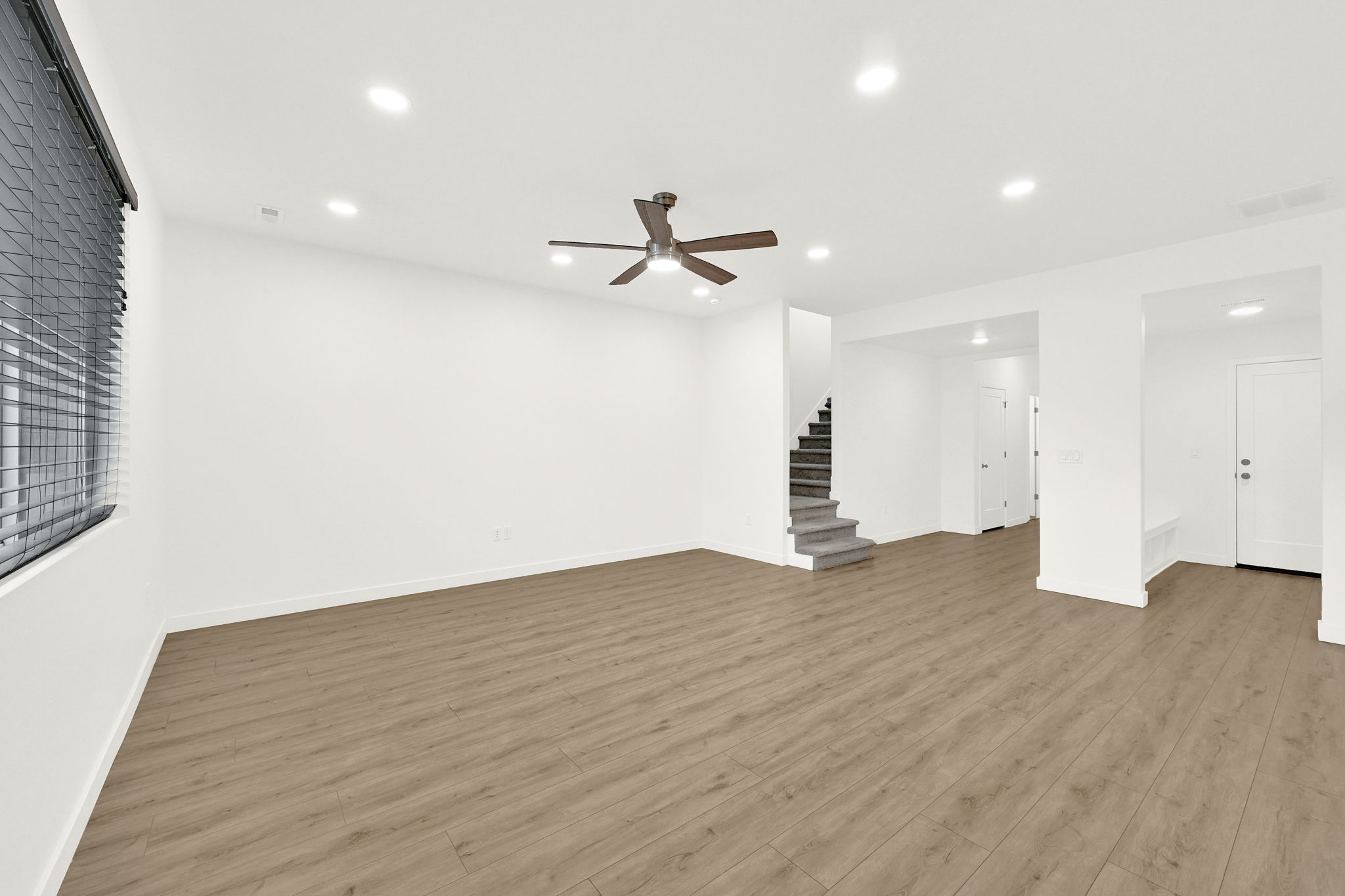 Spacious main living area featuring wood-finish flooring, a ceiling fan with integrated lighting, recessed overhead lighting, and window blinds