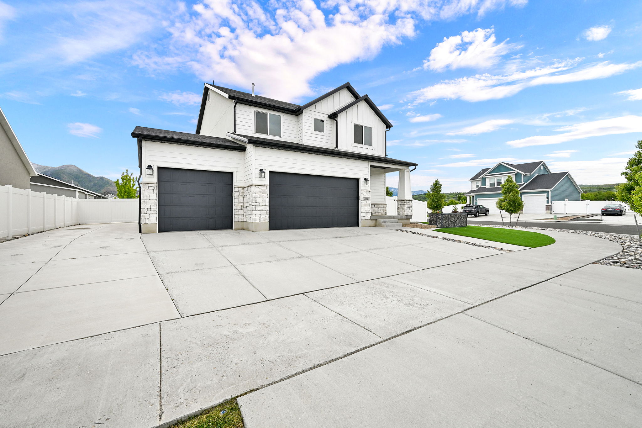 Two-story residence featuring white siding and black trim, a prominent two-car garage with dark doors, a covered entry porch, white stone accents on the facade, and a wide concrete driveway