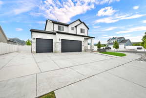 Two-story residence featuring white siding and black trim, a prominent two-car garage with dark doors, a covered entry porch, white stone accents on the facade, and a wide concrete driveway