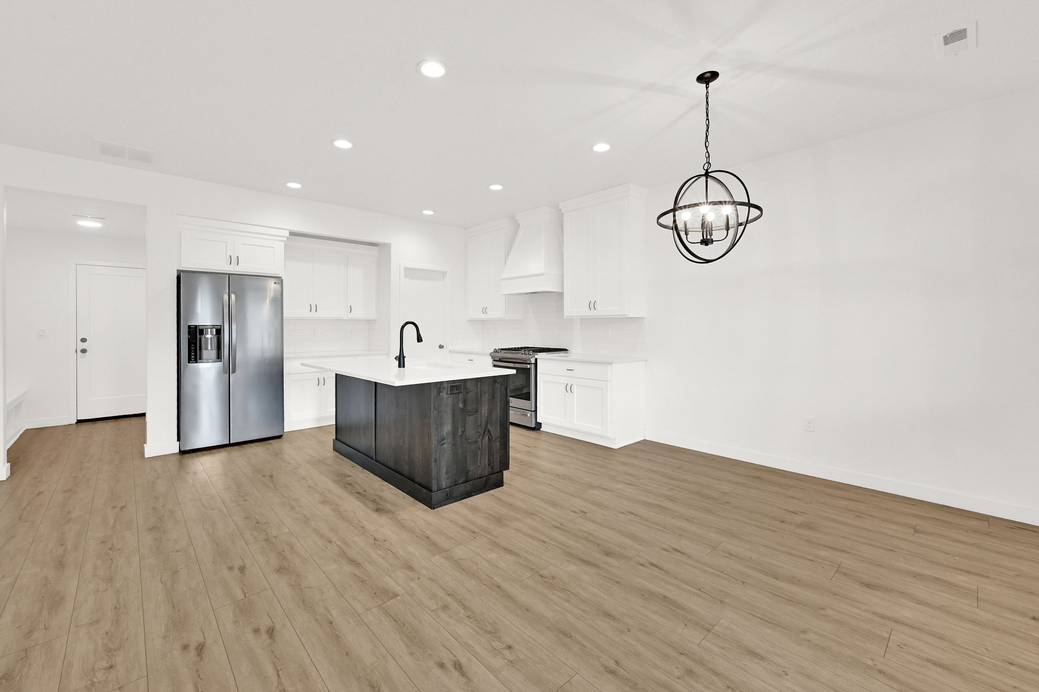 Open-concept kitchen and living area featuring wood-finish flooring, white cabinetry, a dark wood-finish island with a white countertop, and stainless steel appliances