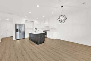 Open-concept kitchen and living area featuring wood-finish flooring, white cabinetry, a dark wood-finish island with a white countertop, and stainless steel appliances