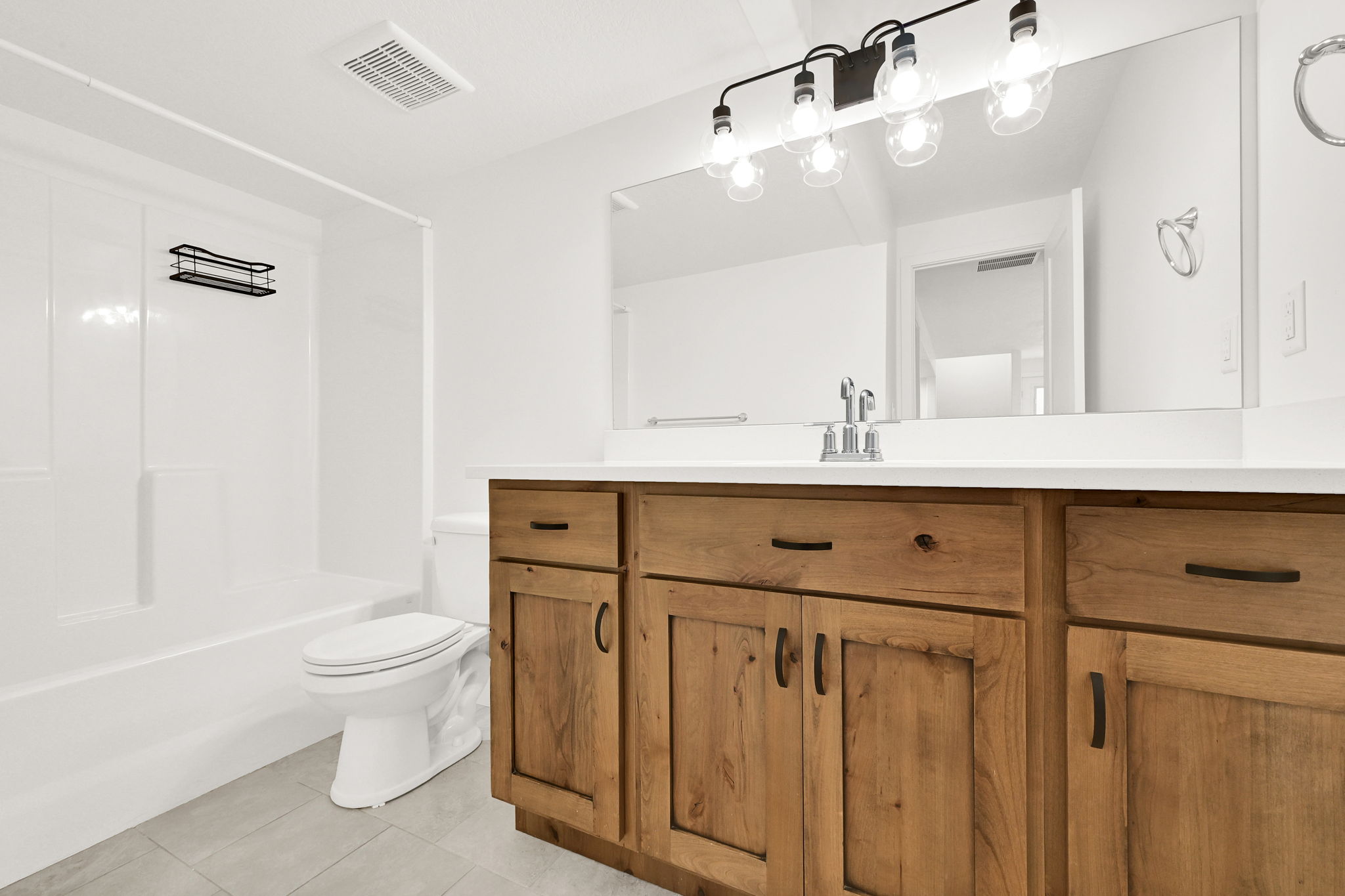 Bathroom featuring a wide wood-finish vanity with a light-colored countertop, large wall-mounted mirror, and a 4-light fixture with clear glass globes