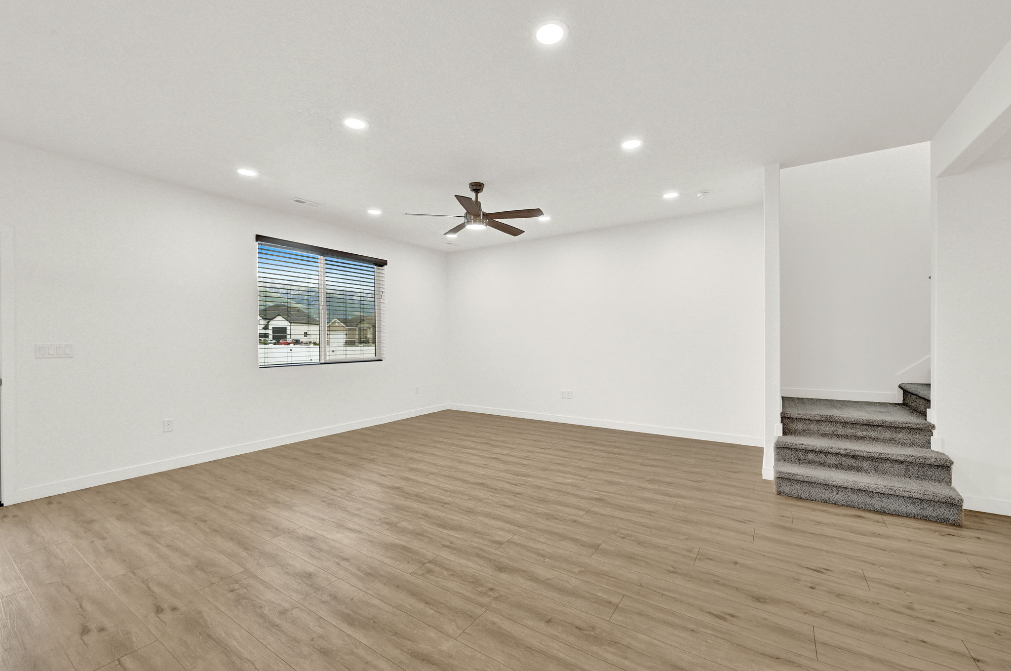 Spacious room featuring wood-finish flooring, white walls, and a ceiling fan