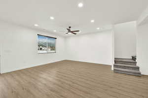 Spacious room featuring wood-finish flooring, white walls, and a ceiling fan