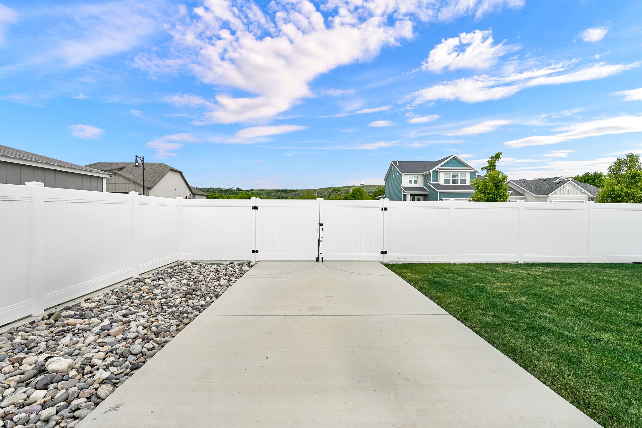 Expansive fenced backyard featuring a concrete patio, a gravel border, and a manicured lawn
