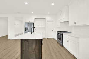 Modern kitchen featuring a large island with a black faucet, stainless steel appliances, white cabinetry, a subway tile backsplash, and light wood-finish flooring