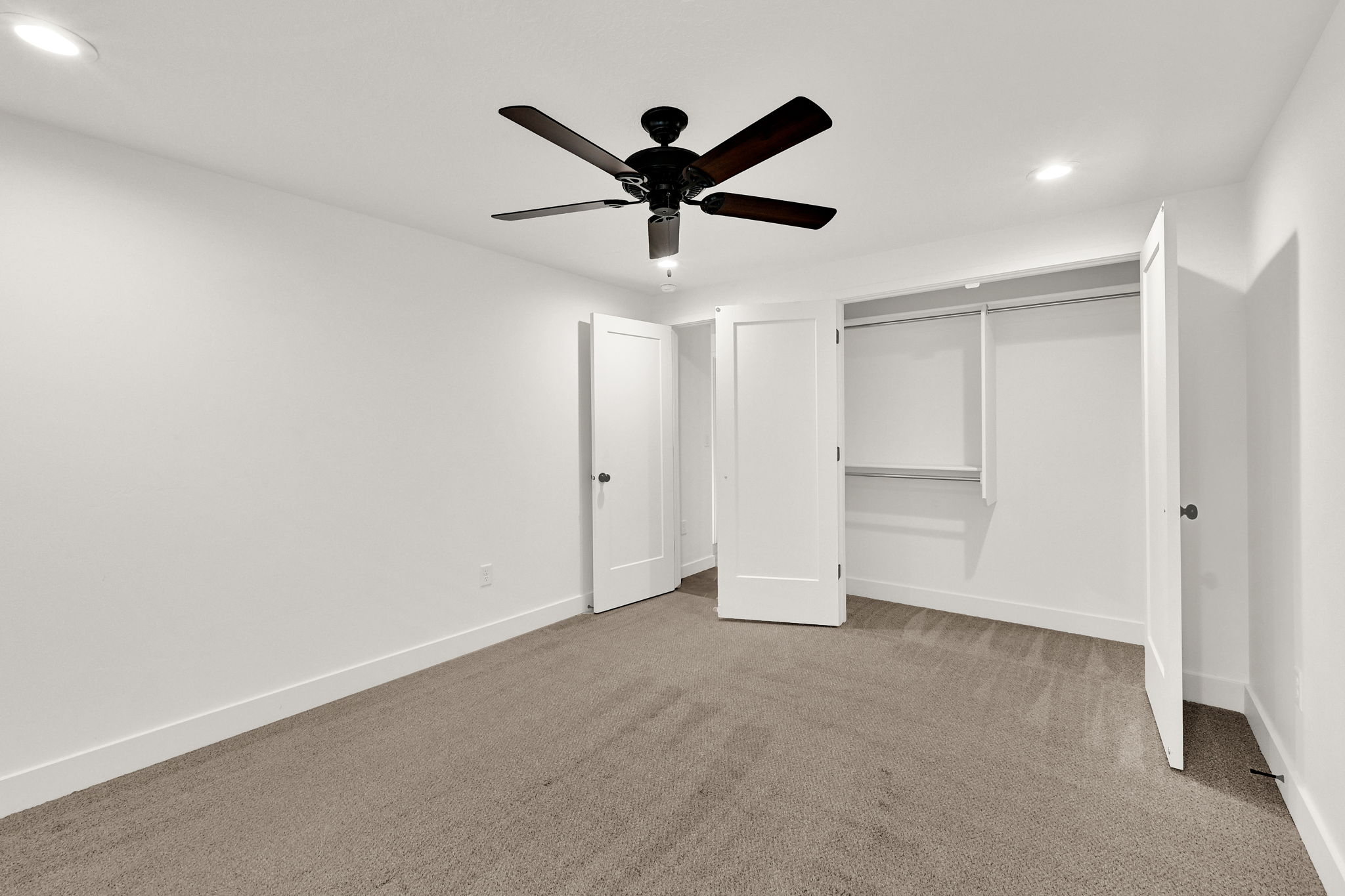 Spacious room featuring neutral carpet flooring, recessed lighting, a ceiling fan with dark wood-finish blades, and a built-in closet with shelving and hanging rods