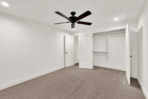 Spacious room featuring neutral carpet flooring, recessed lighting, a ceiling fan with dark wood-finish blades, and a built-in closet with shelving and hanging rods