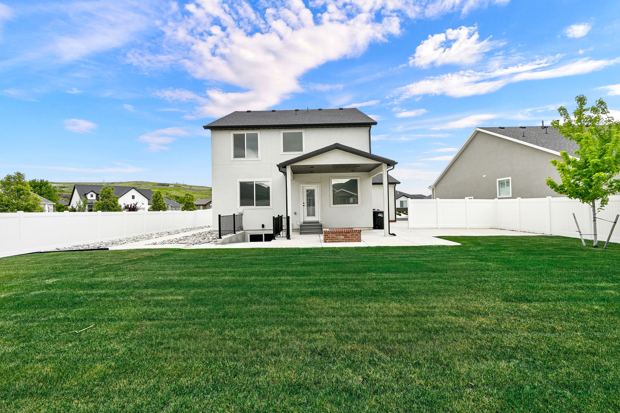 Expansive rear yard featuring a large grass lawn, a white privacy fence, and a concrete patio