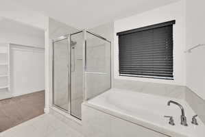 Spacious bathroom featuring a built-in soaking tub, a separate glass-enclosed shower, polished chrome fixtures, and marble-look tile flooring and surrounds
