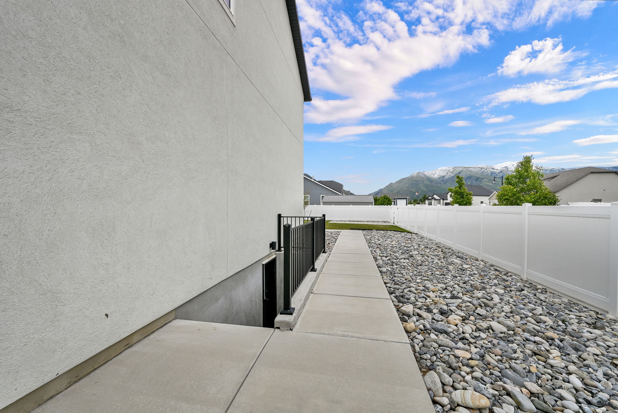 Stucco exterior with a concrete walkway, rock landscaping, and a white privacy fence
