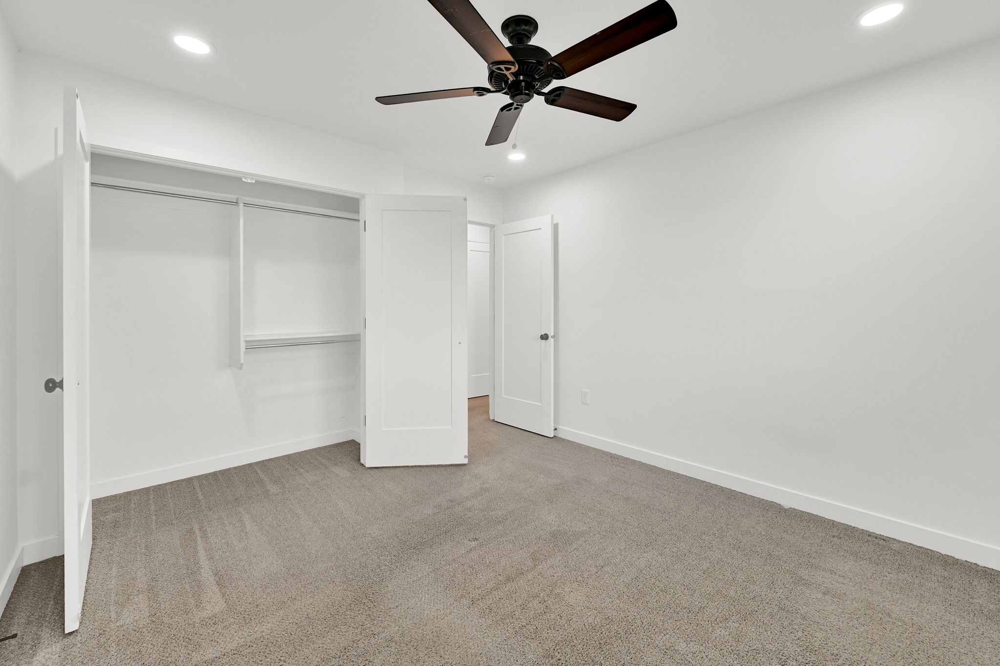 Spacious room featuring neutral carpeting, recessed lighting, and a ceiling fan with dark wood-finish blades