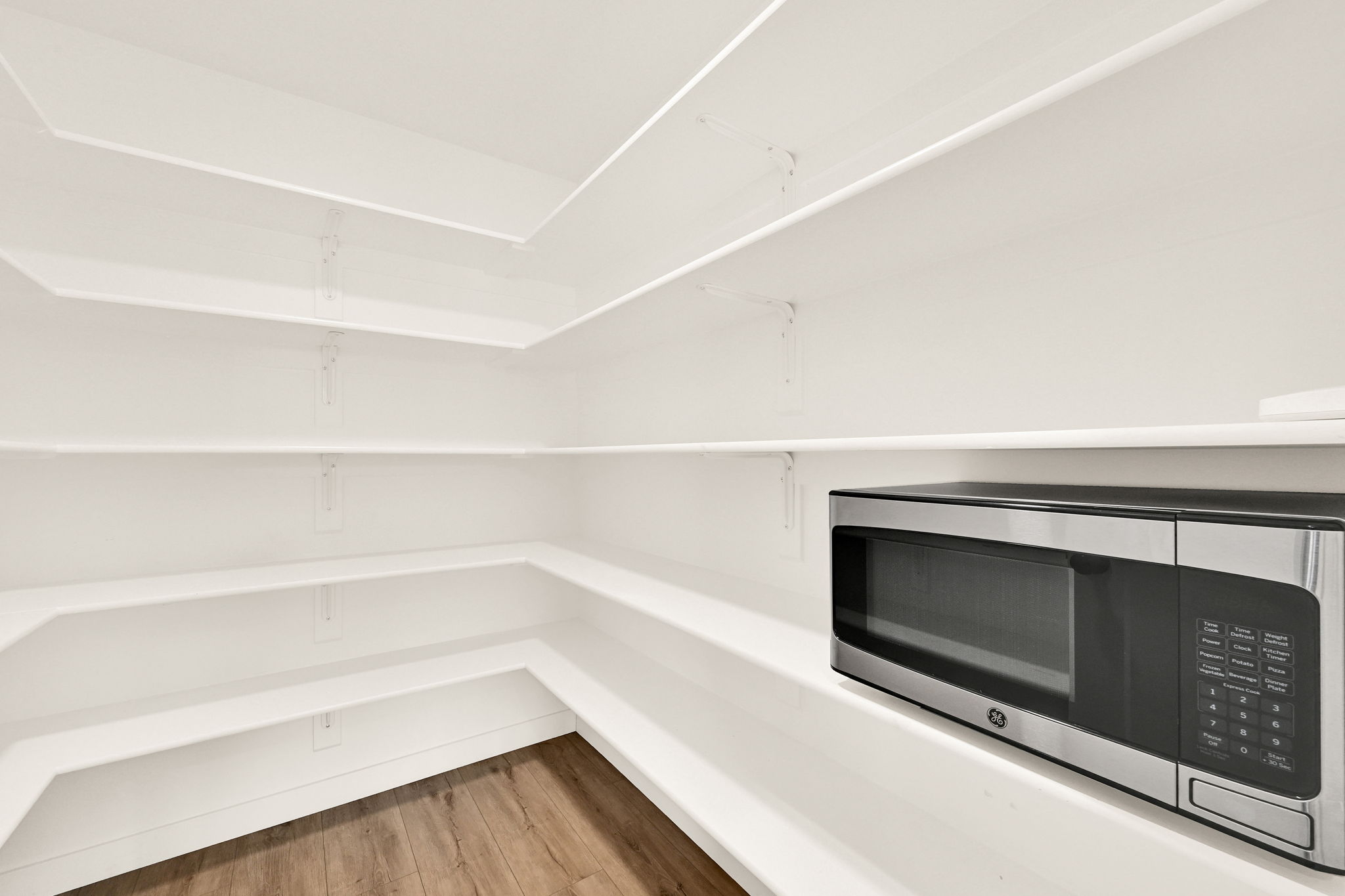 Spacious pantry featuring white shelving, wood-finish flooring, and a built-in microwave