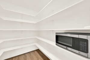 Spacious pantry featuring white shelving, wood-finish flooring, and a built-in microwave
