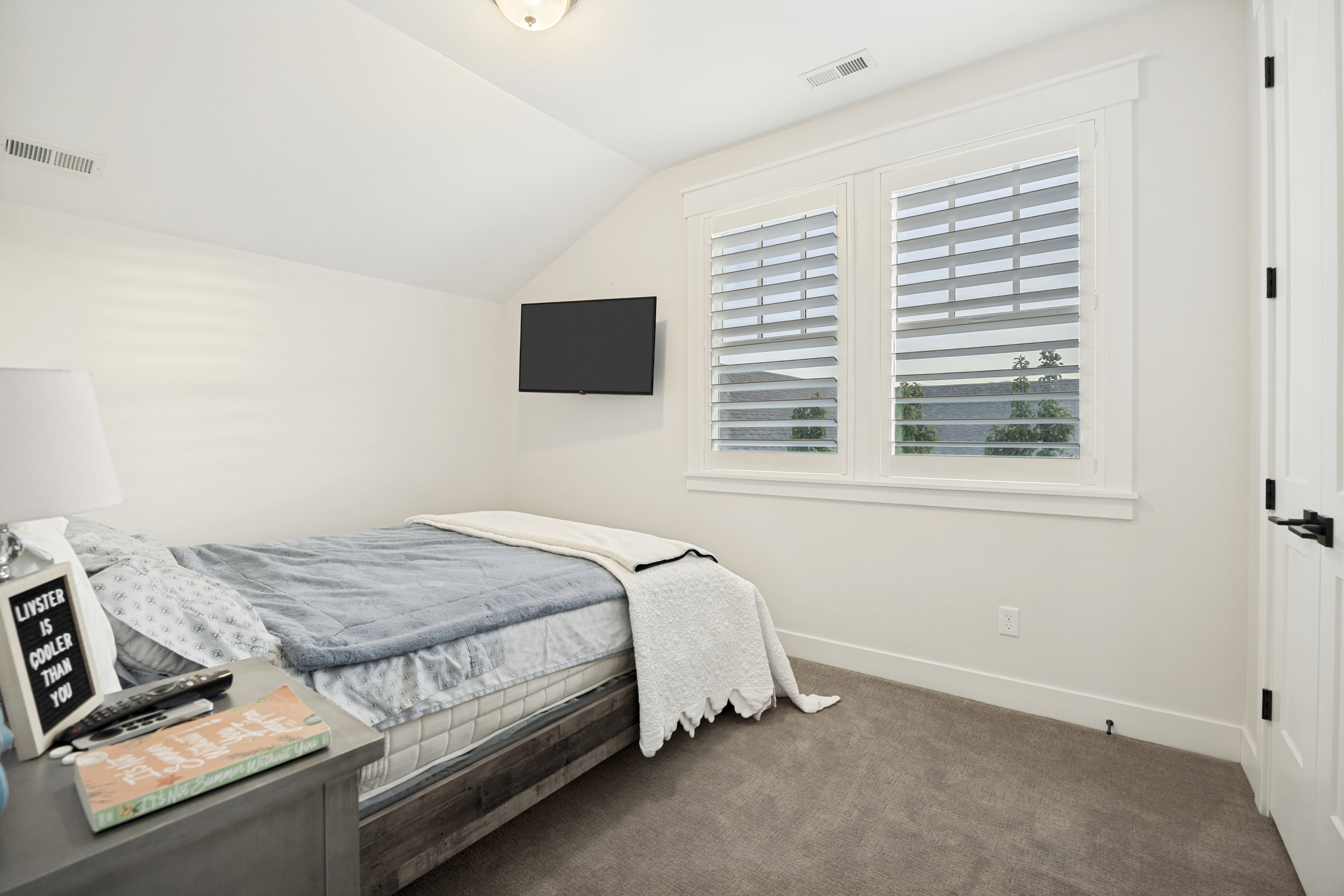 Light-filled room featuring white walls, gray carpet, and a window with plantation shutters