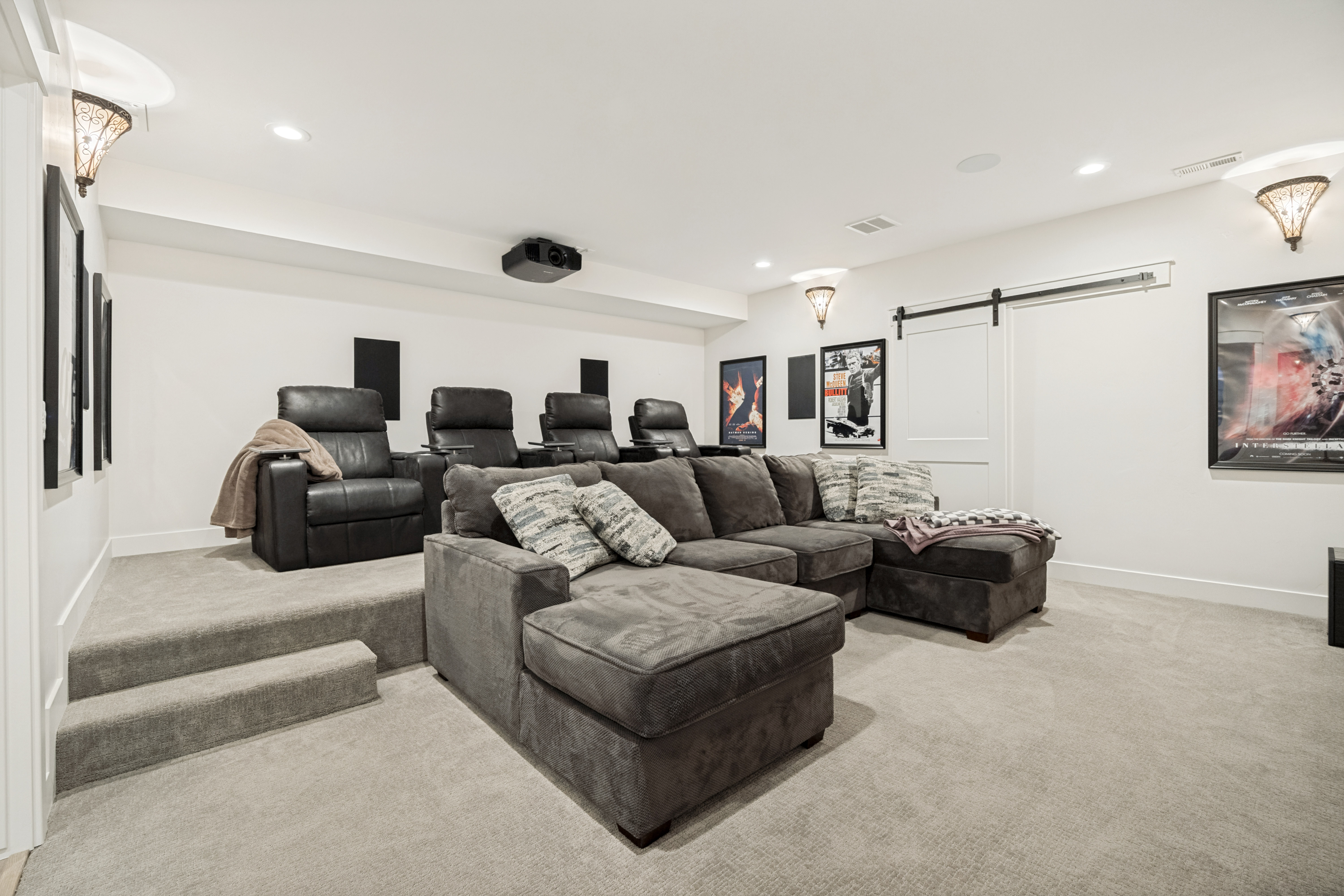 Dedicated media room featuring tiered seating, built-in projector, recessed lighting, wall sconces, and barn door entry