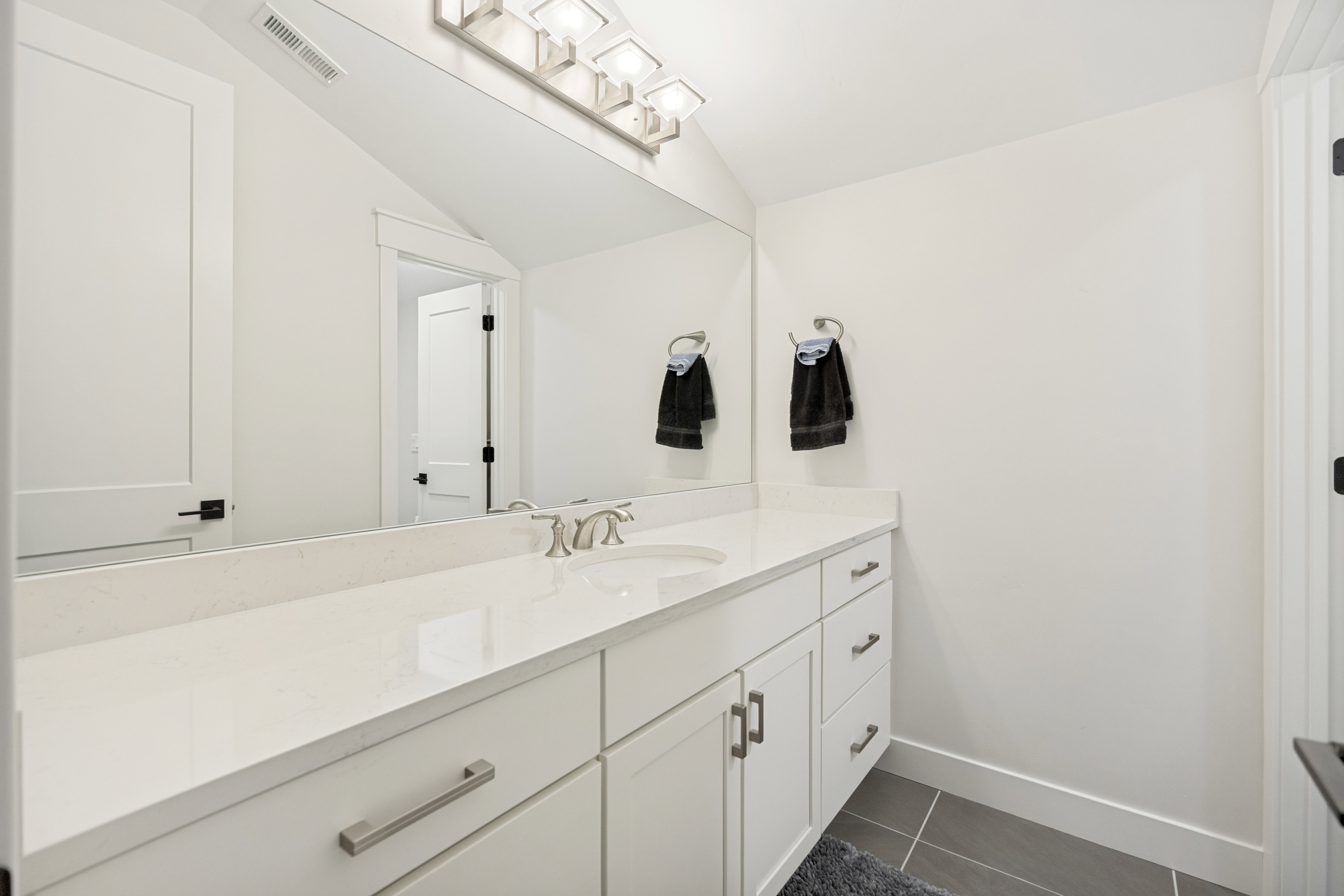 Modern bathroom vanity featuring a white countertop with integrated sink, brushed nickel faucet, and a large mirror