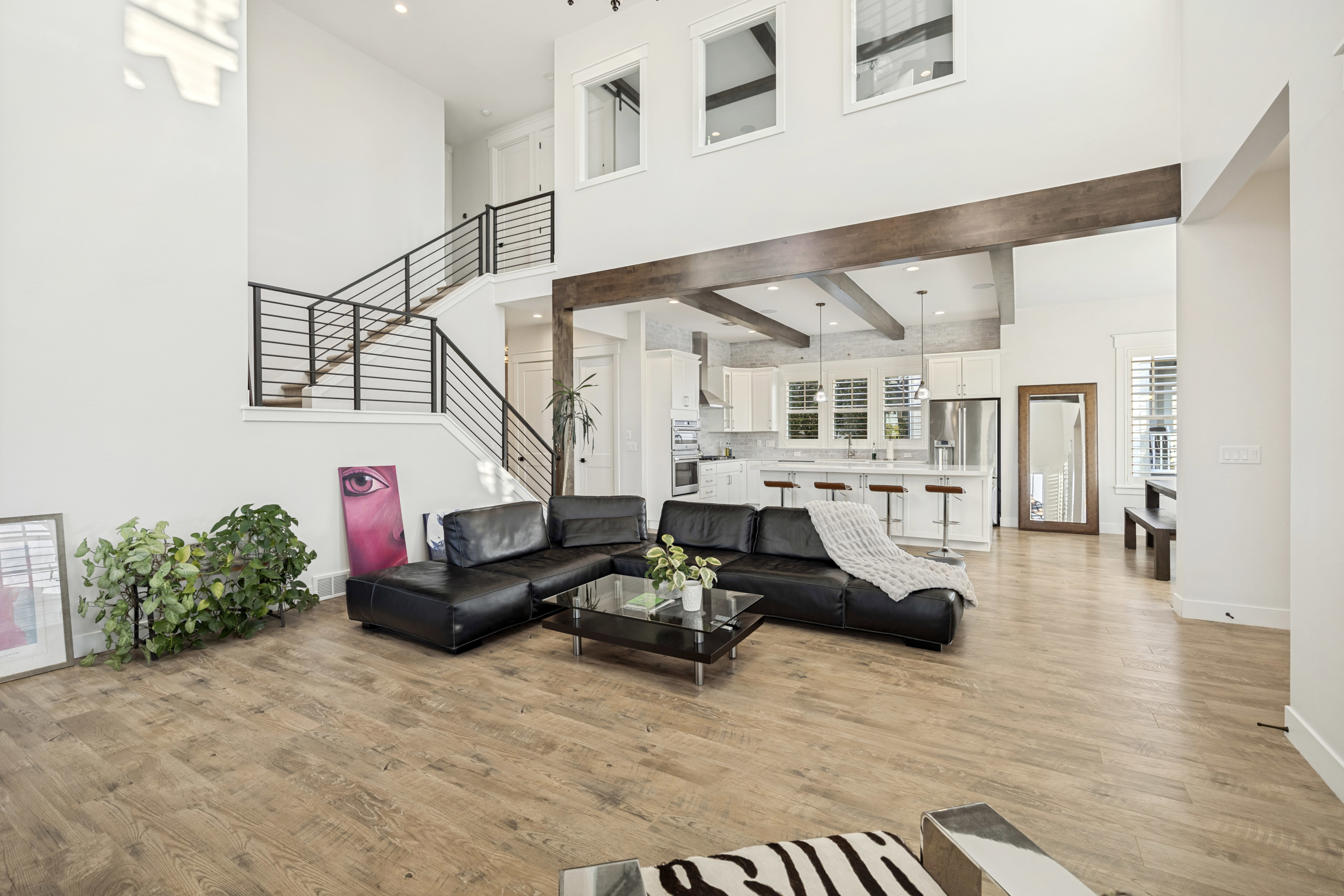 Open-concept living space with wood-finish flooring, a contemporary staircase featuring metal railings, and high ceilings