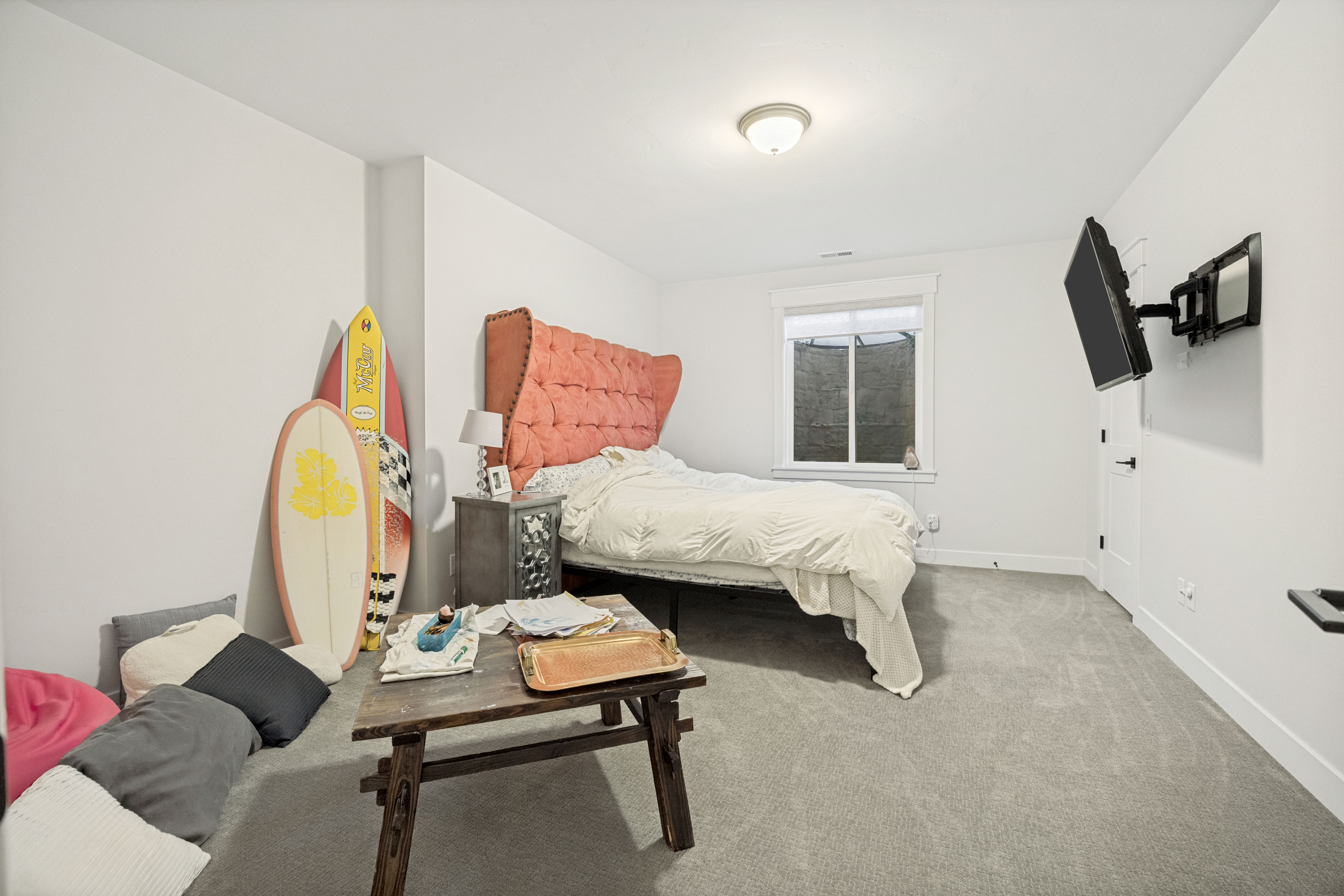 Spacious room featuring light gray carpeting, crisp white walls, a white-framed window, and a white interior door with matte black hardware