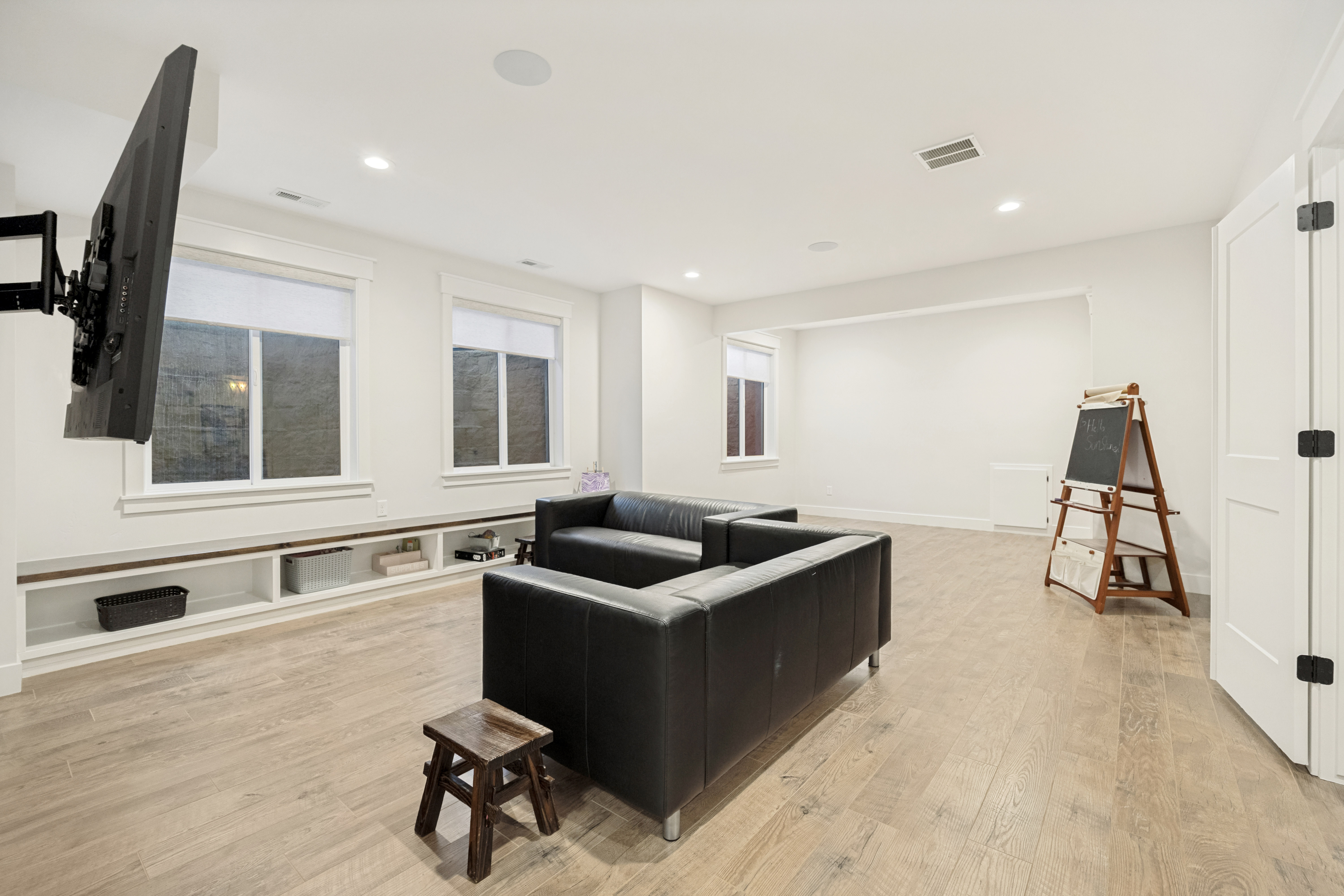 Spacious room featuring light wood-finish flooring, recessed lighting, and a built-in media console with open shelving
