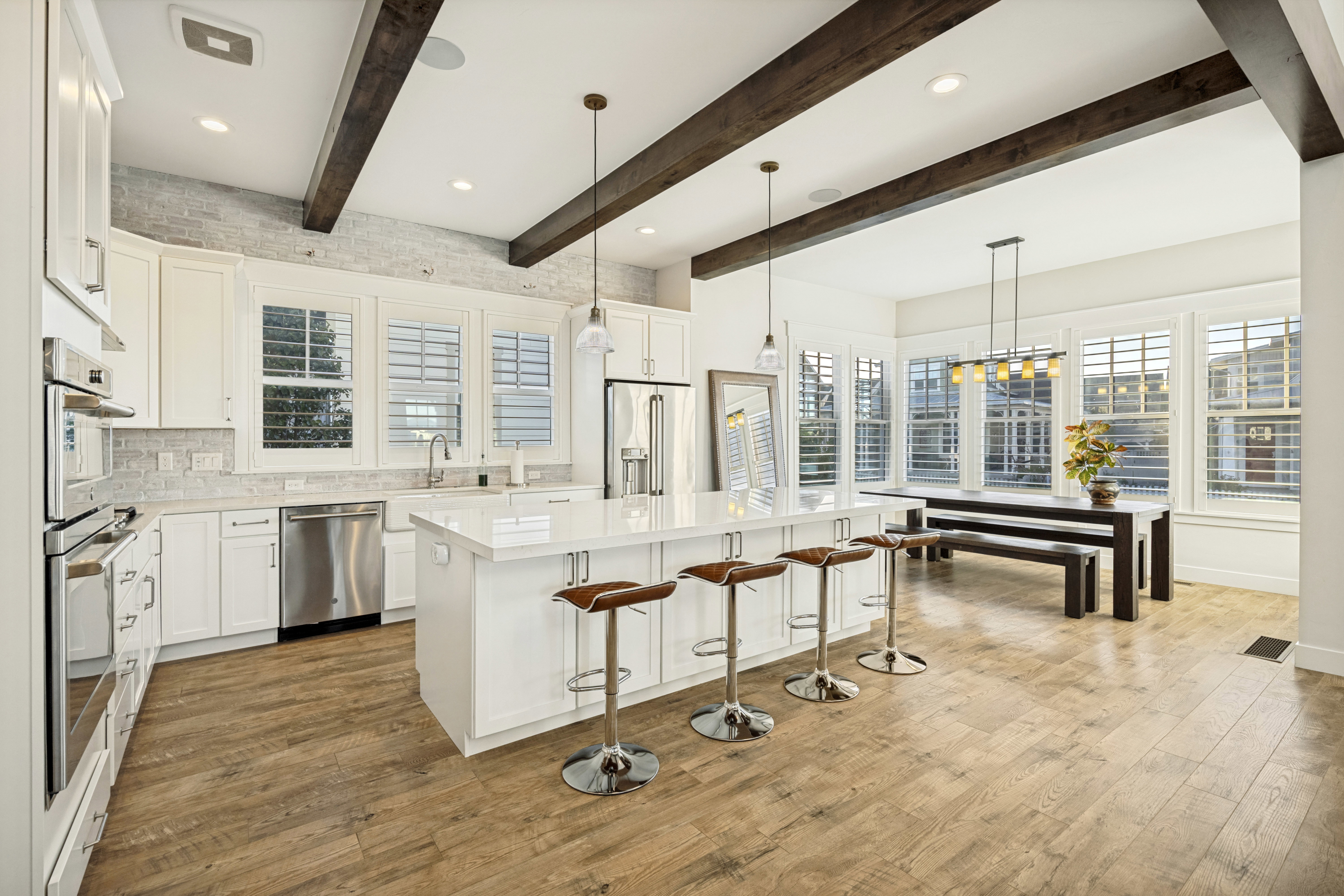 Open-concept kitchen and dining area featuring wood-finish flooring, exposed ceiling beams, white cabinetry, a large kitchen island with seating, and stainless steel appliances